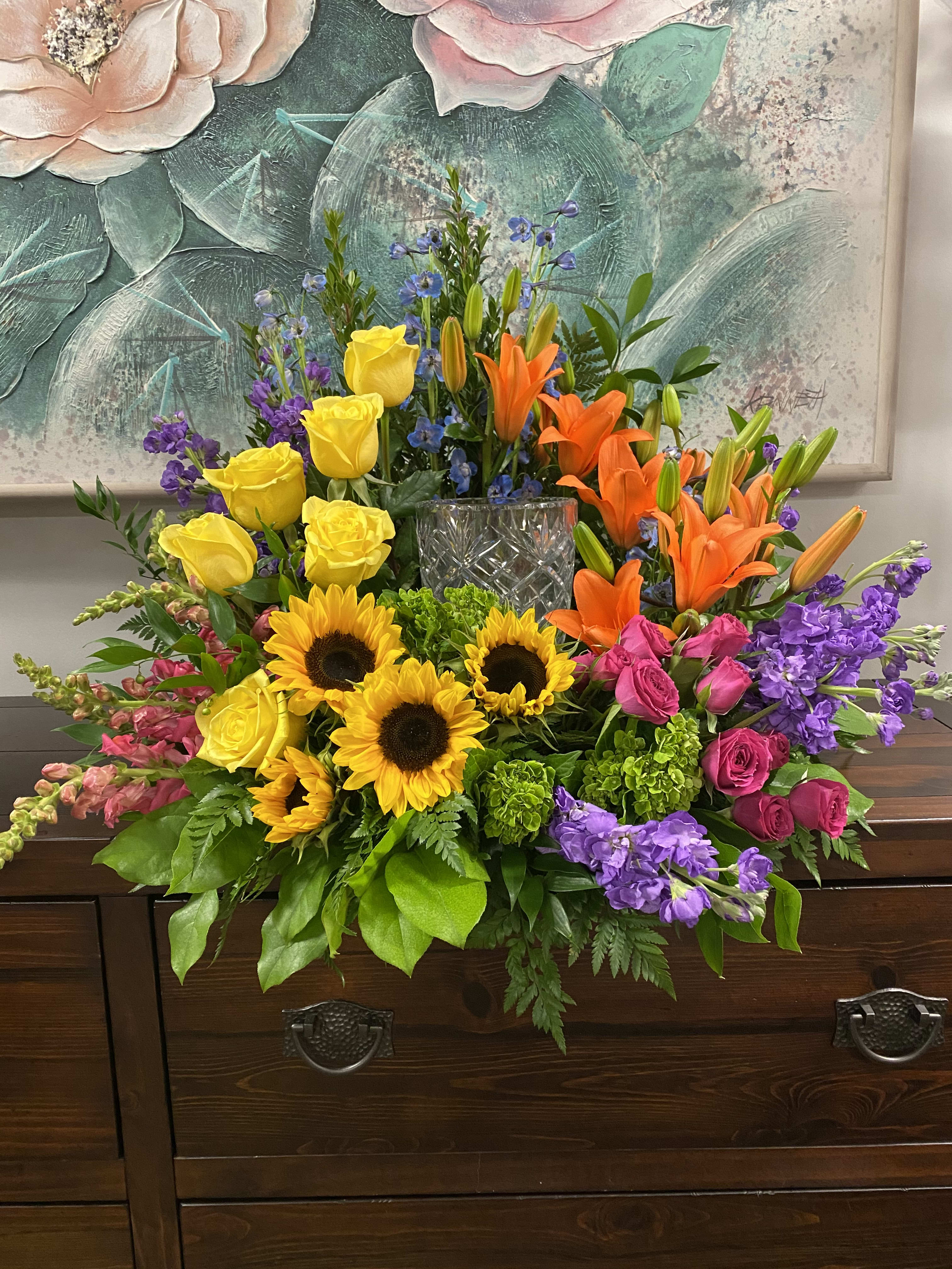 Colorful mixed bouquet with sunflowers, roses, lilies, and purple blooms in a glass vase