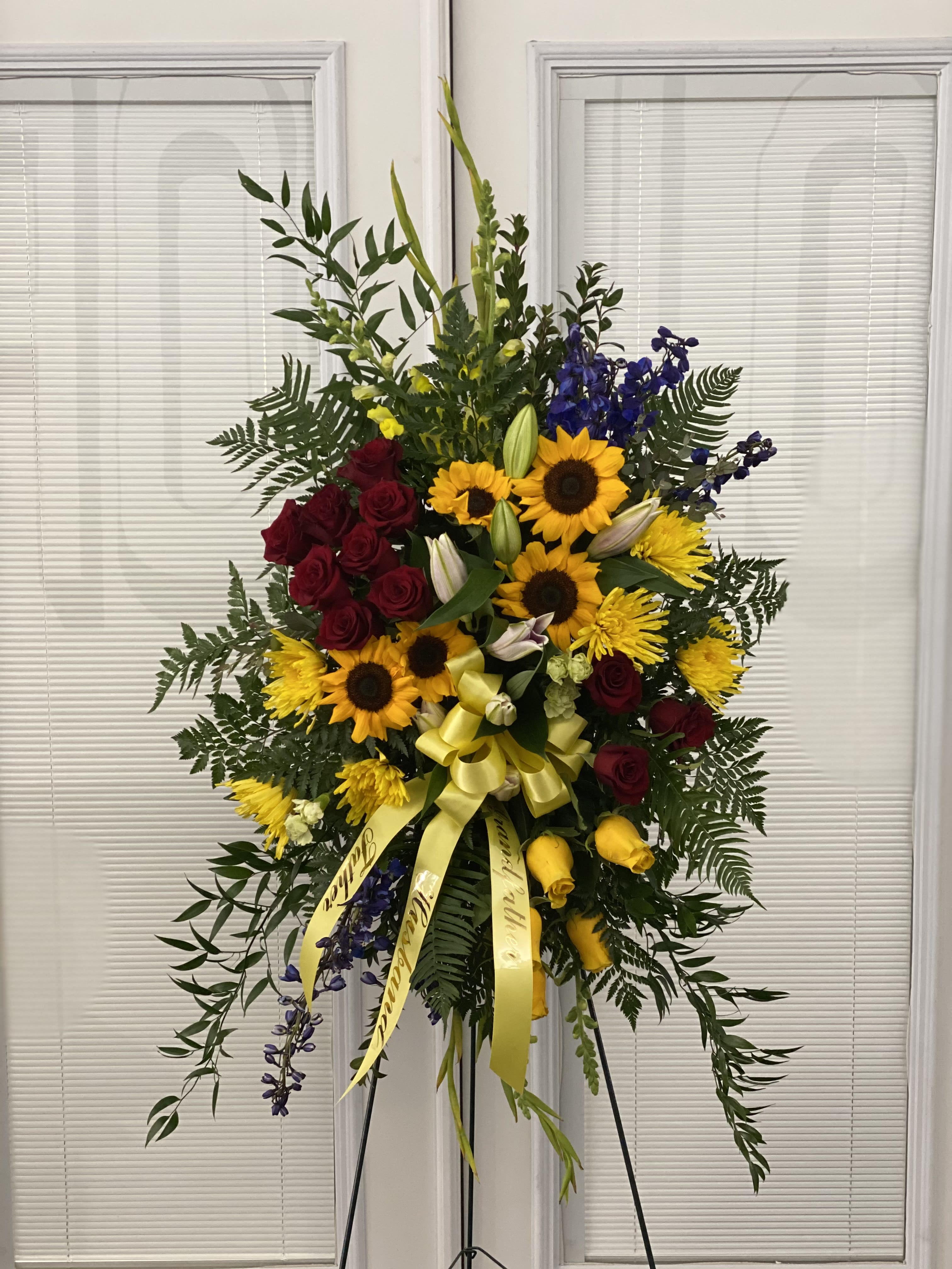 Standing floral spray with red roses, sunflowers, and yellow ribbon