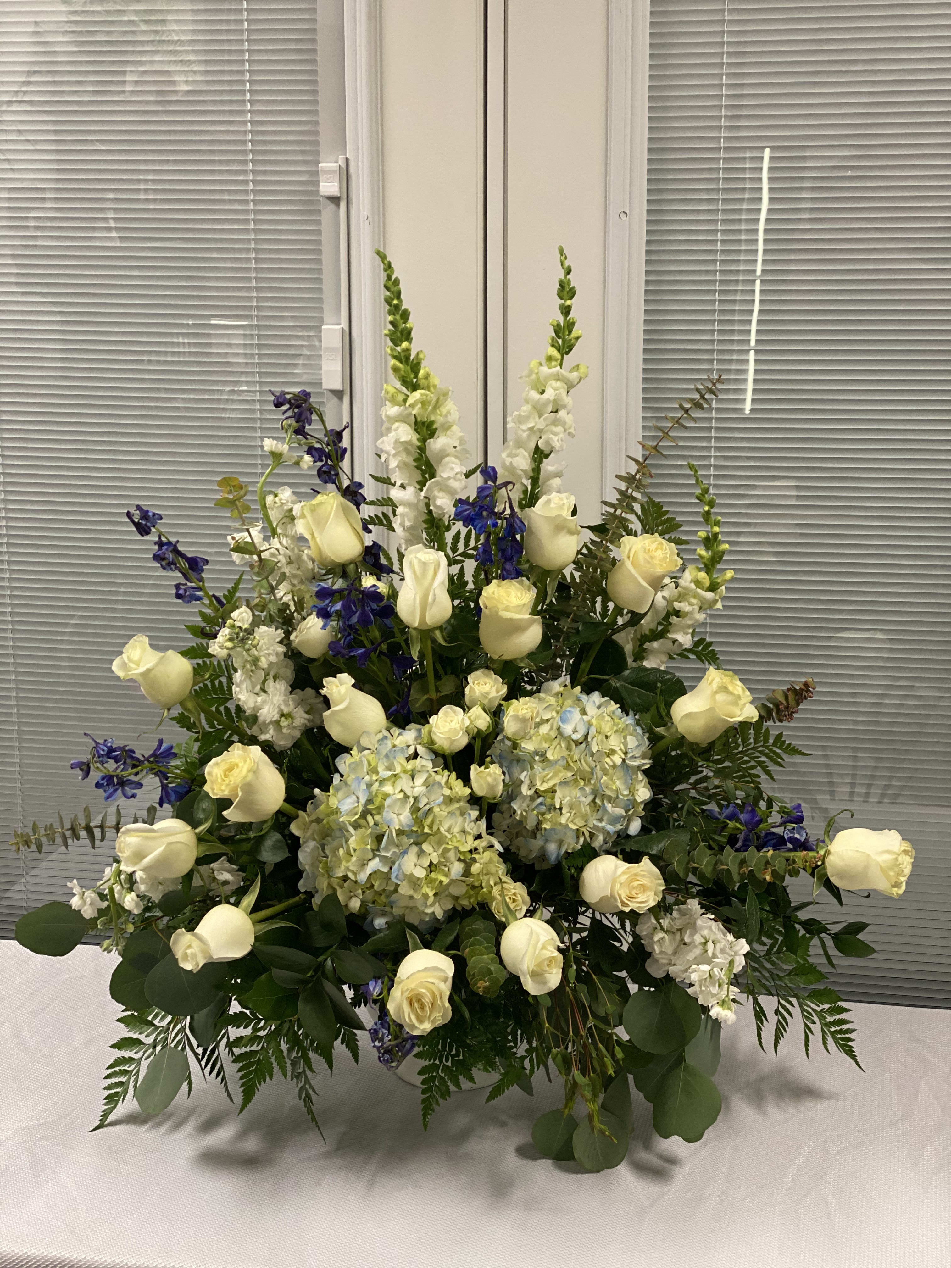 Large floral arrangement with white roses, blue flowers, and pale hydrangeas