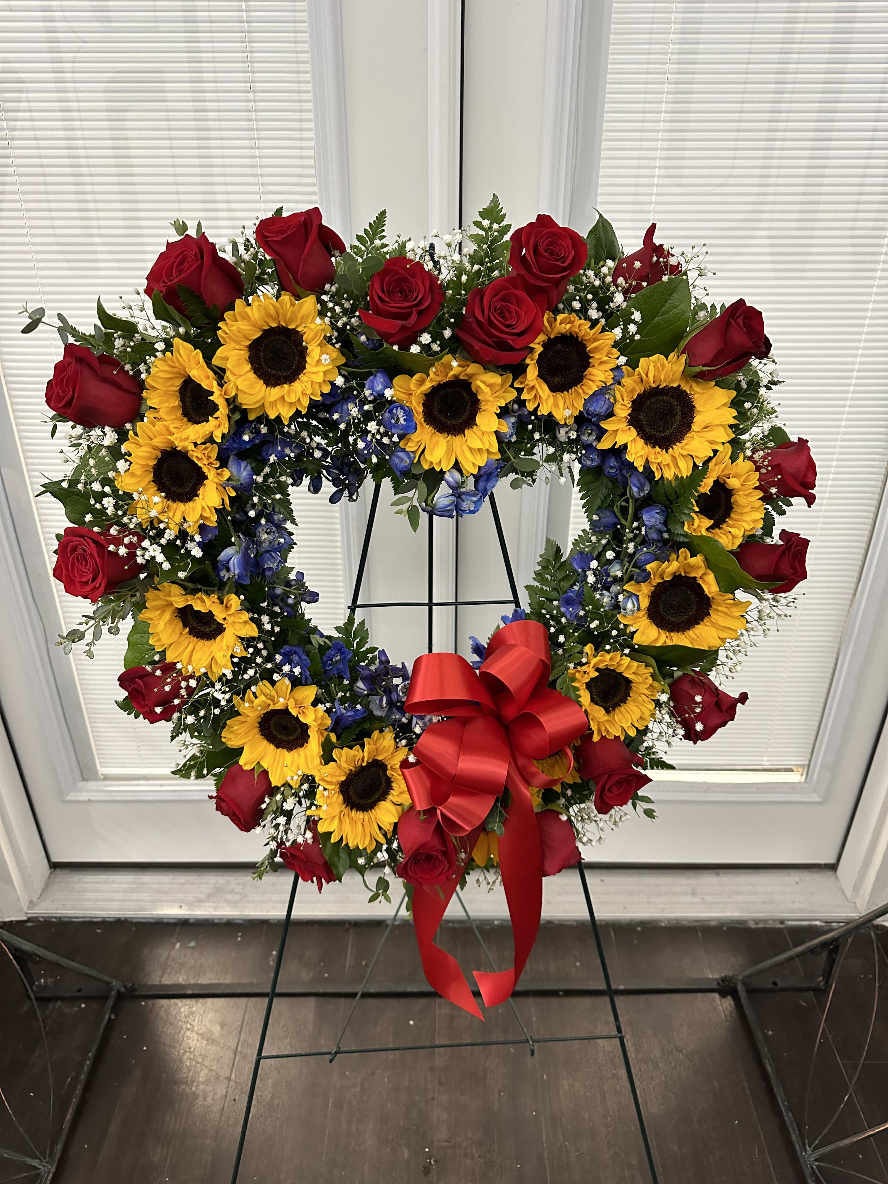 Heart-shaped wreath of red roses and sunflowers with a red bow