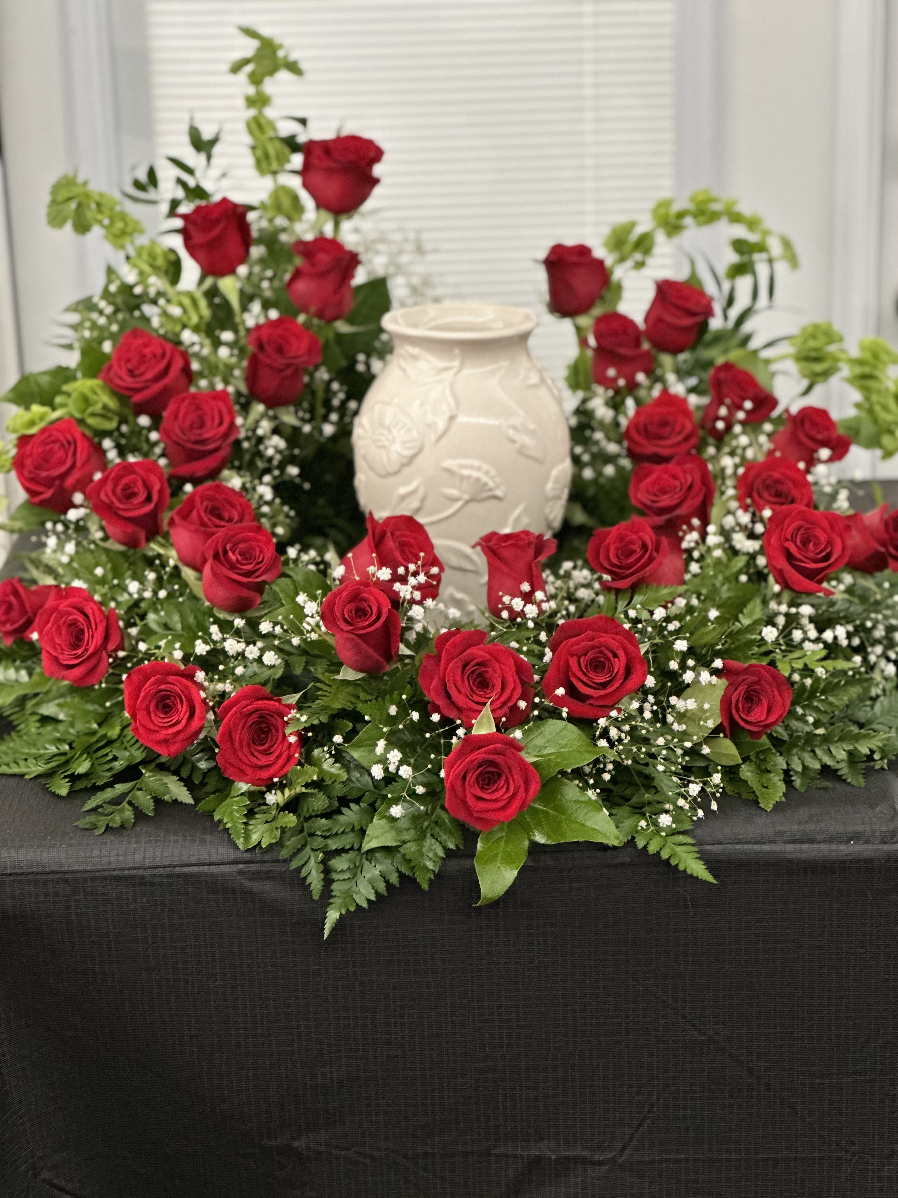 Red roses arranged around a white vase centerpiece