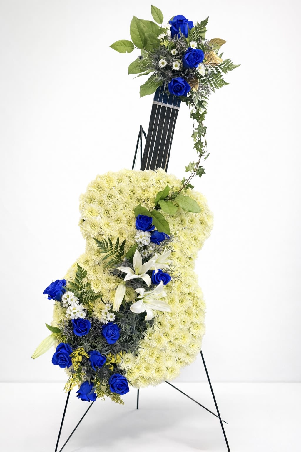 Blue Tribute Guitar - Funeral arrangement in a guitar shape, crafted with a base of spray mums, accented with blue roses and delicate lilies, complemented by fresh greenery. A special tribute that honors the memory and spirit of a loved one who will always live in our hearts.
