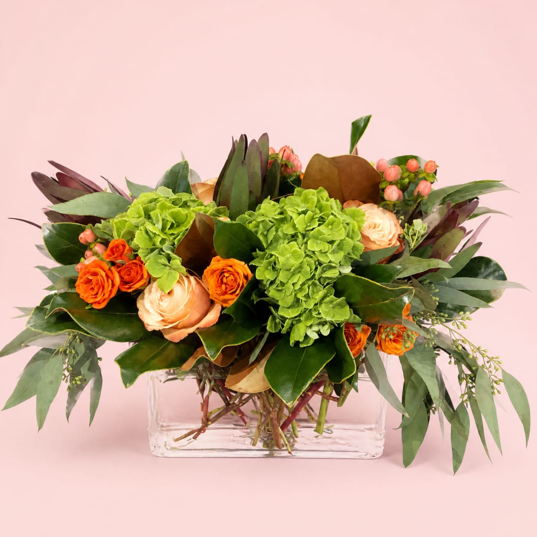 Orange and peach roses with green hydrangeas in a clear glass vase