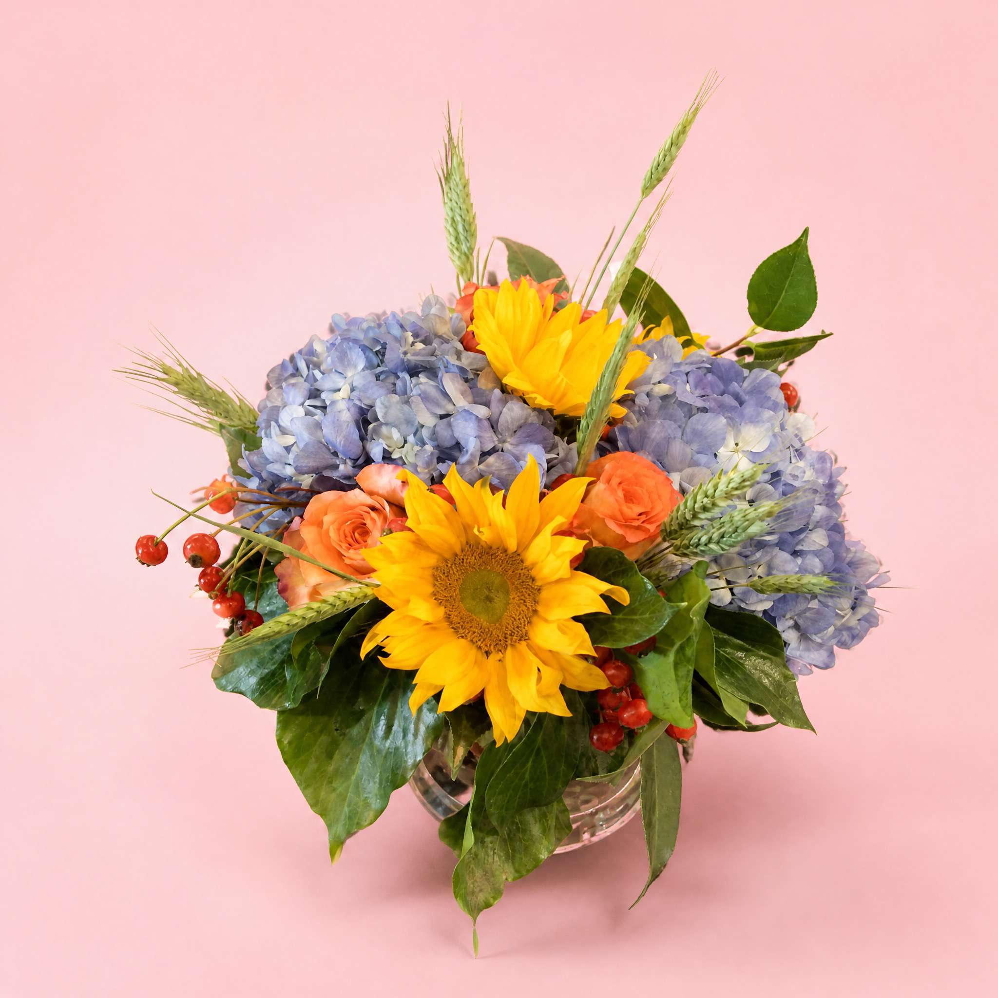 Bouquet of sunflowers, blue hydrangeas, and orange roses in a glass vase