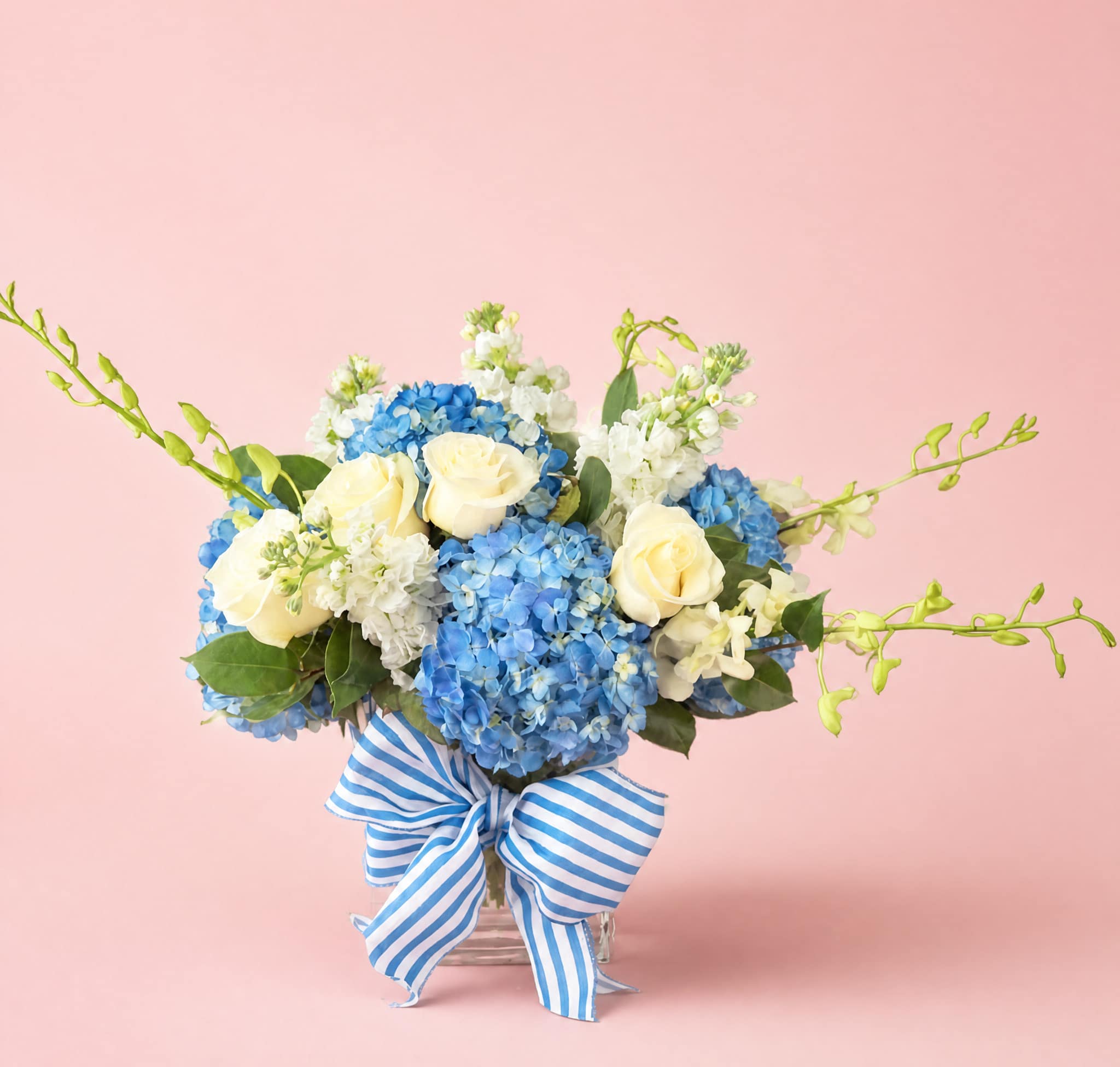 Blue hydrangea and white rose bouquet in a glass vase with a striped ribbon