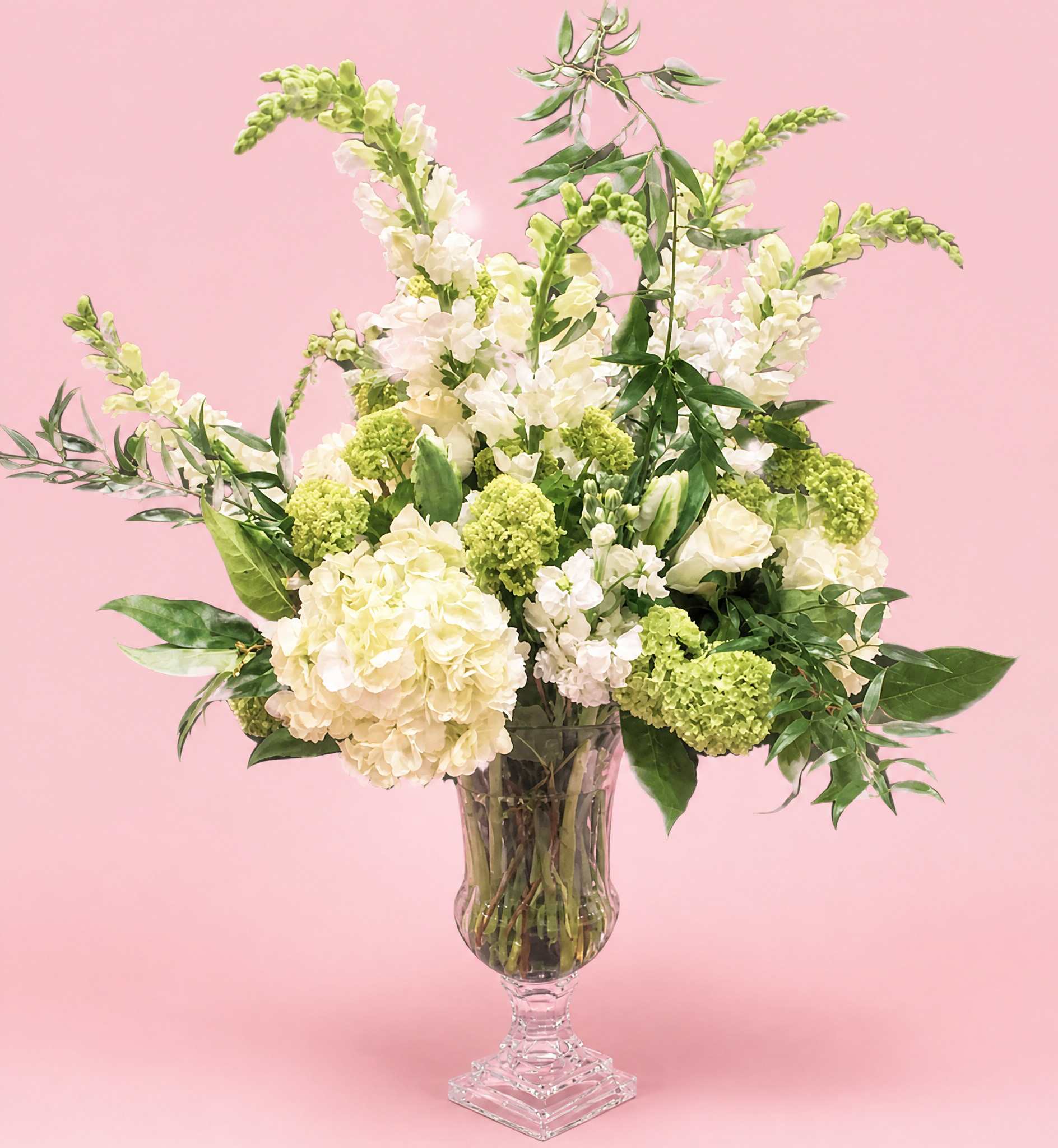 Cream and green floral arrangement in a clear pedestal vase