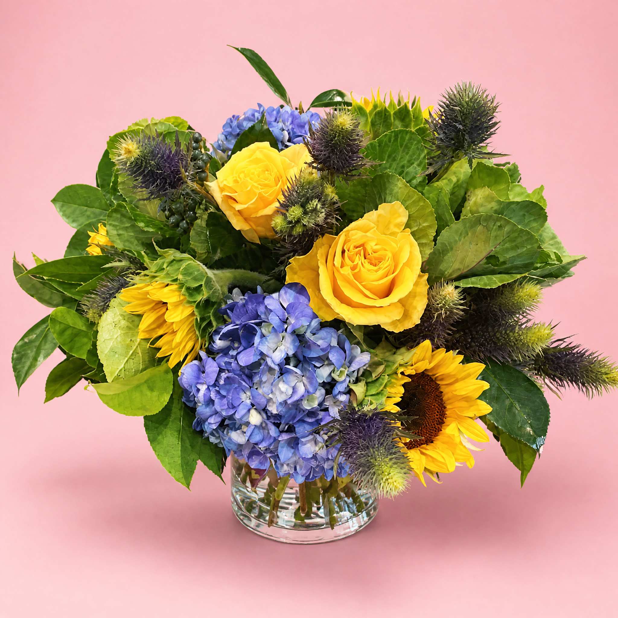 Yellow roses and blue hydrangeas in a clear glass vase