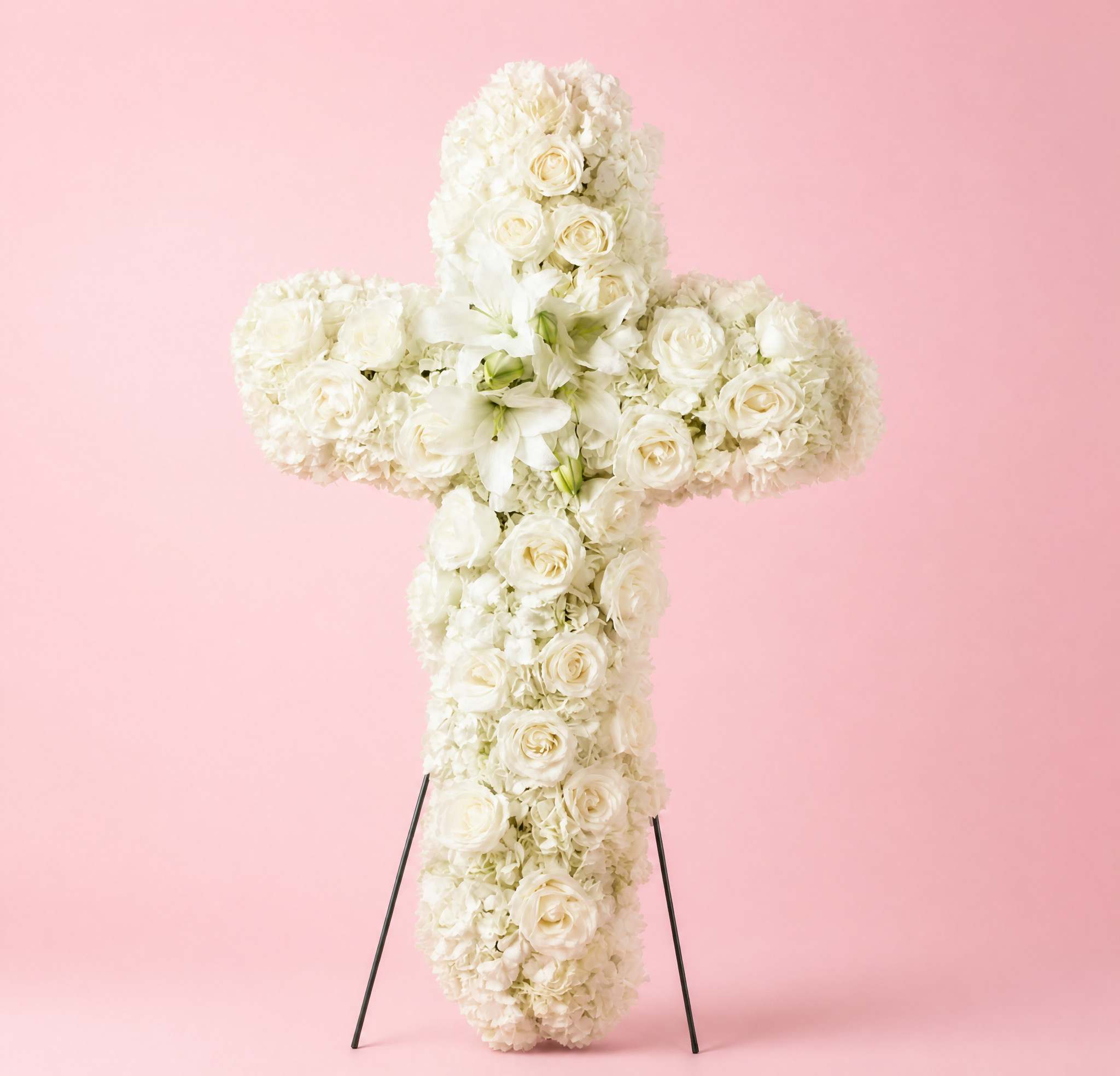White floral cross arrangement on a stand against a pink background