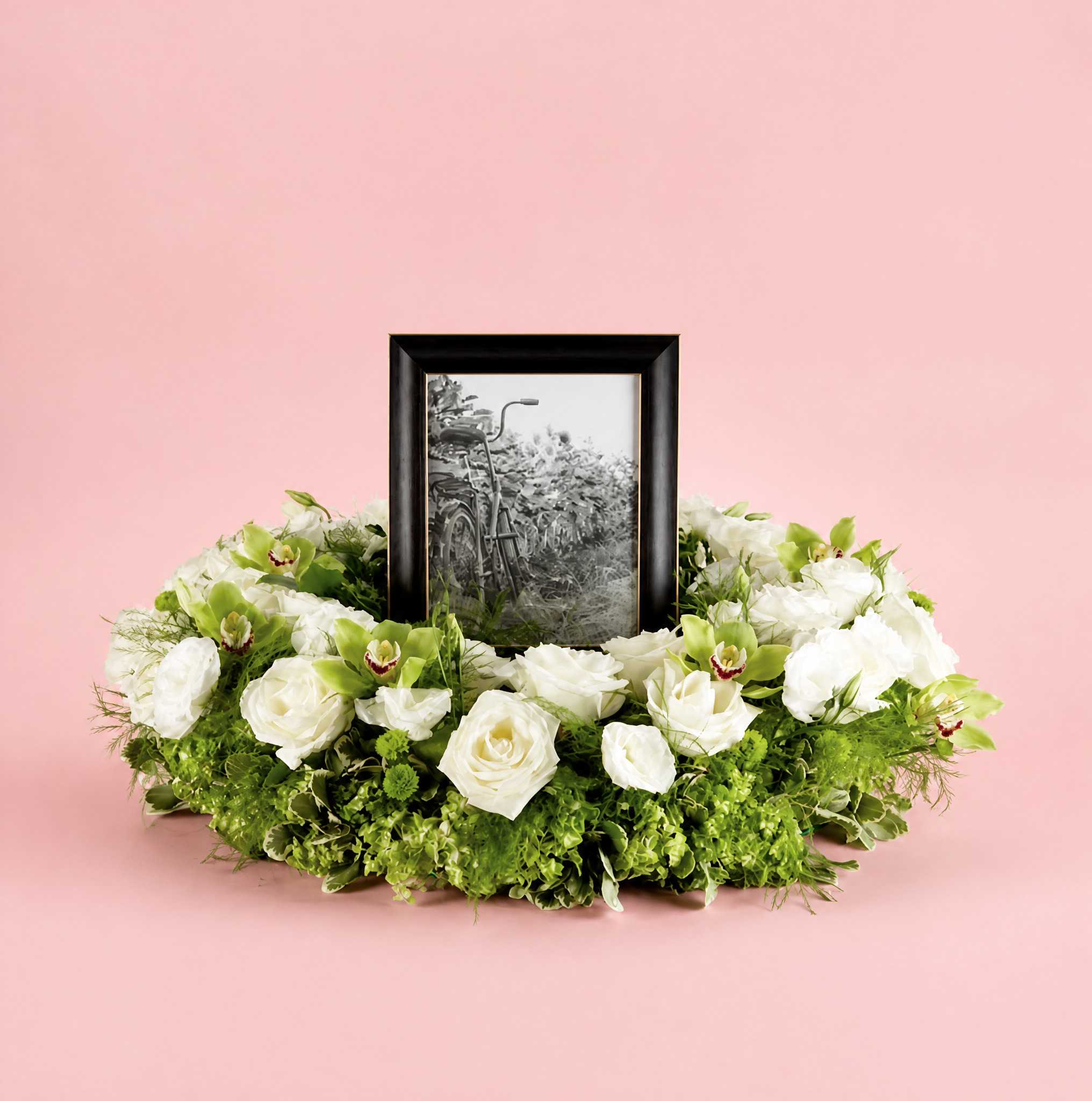 White floral wreath around a framed black-and-white photo on a pink background