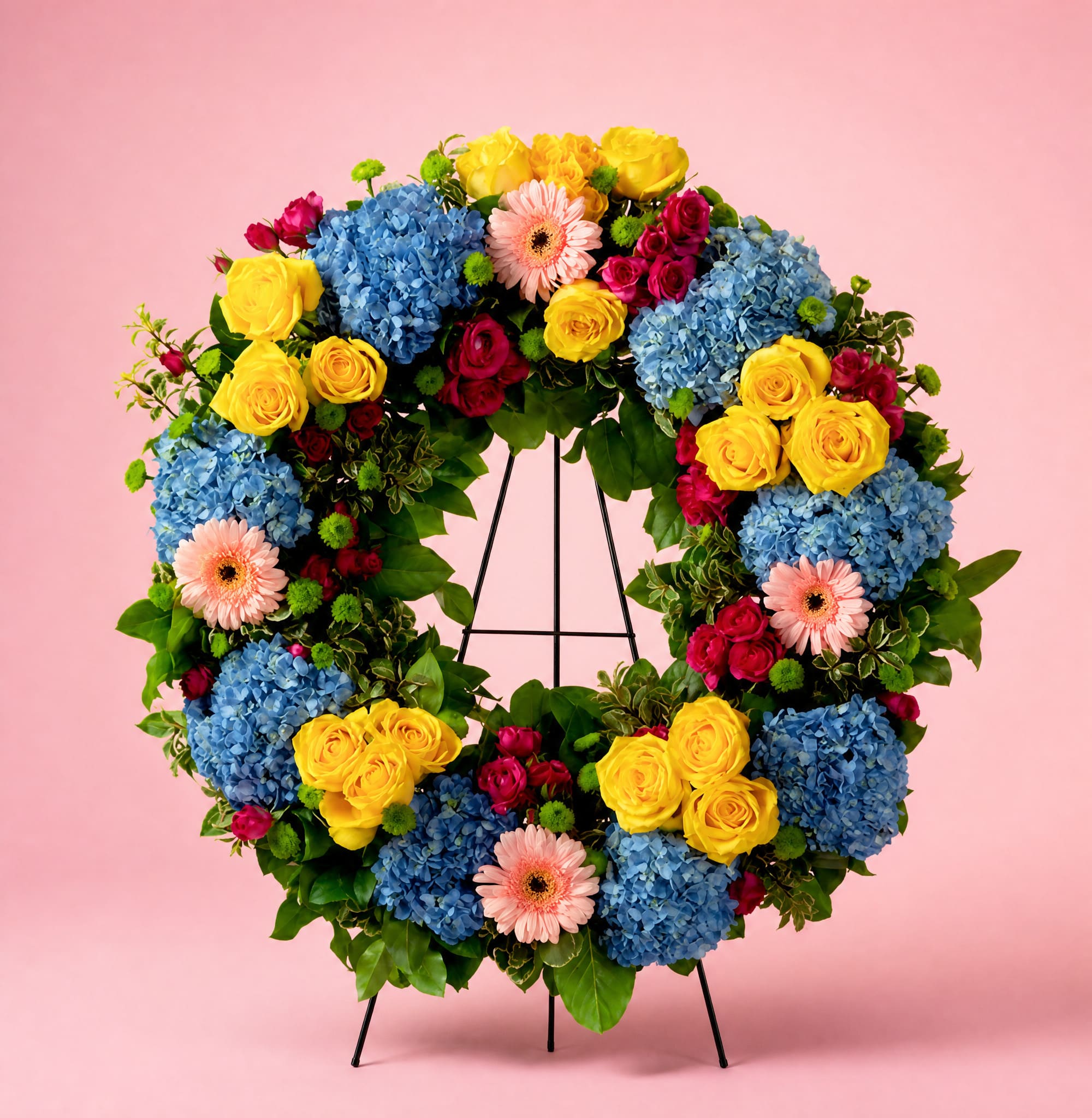 Circular floral wreath with blue hydrangeas, yellow roses, pink gerberas, and red spray roses