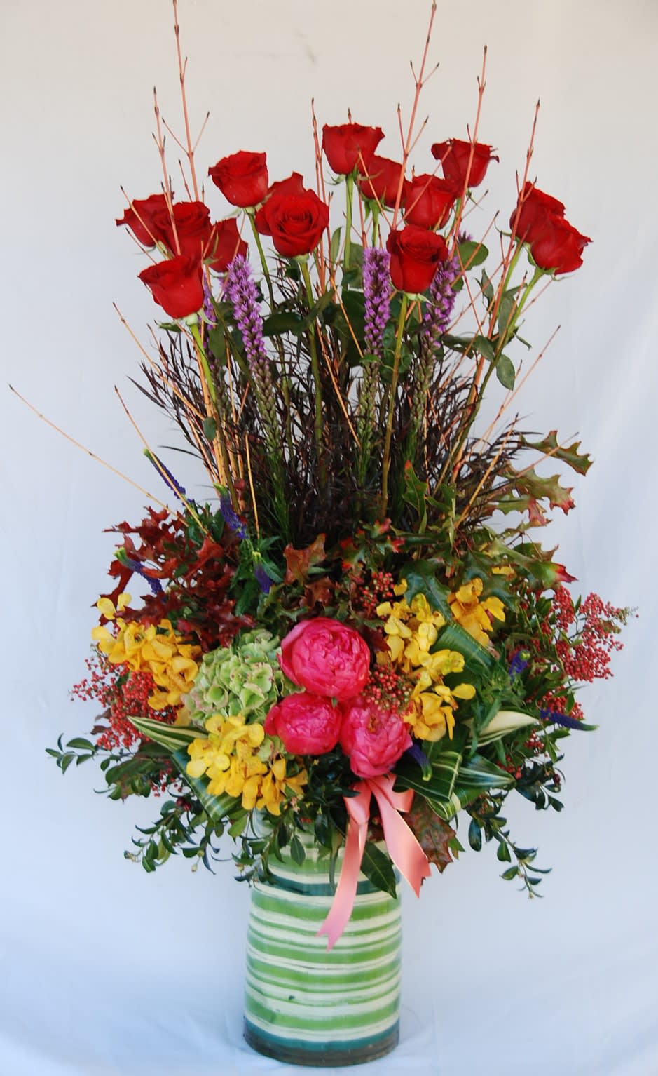 Tall arrangement of red roses, pink blooms, and yellow flowers in a striped vase