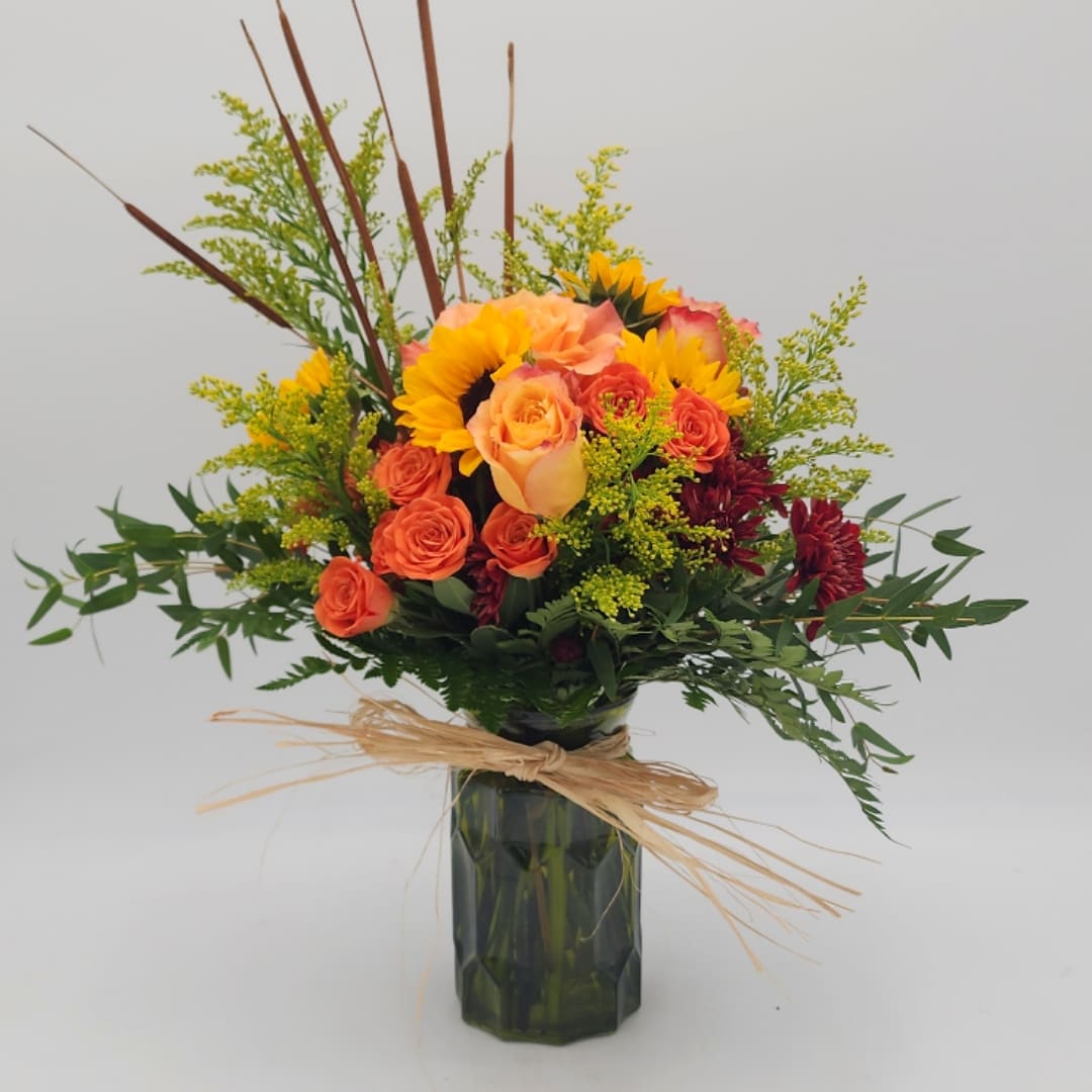 Bouquet of orange roses and sunflowers in a dark glass vase