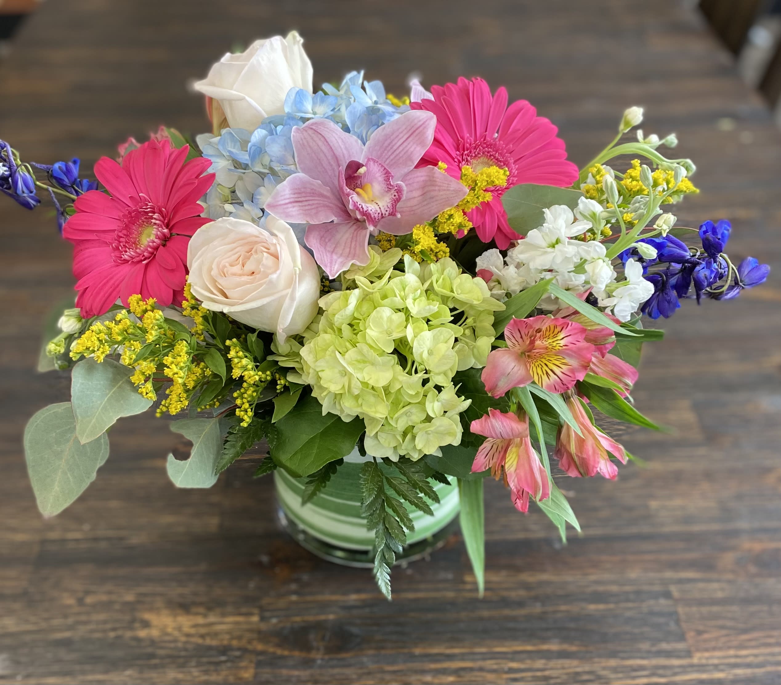 Mixed bouquet in a striped vase with pink daisies, roses, hydrangea, and orchids