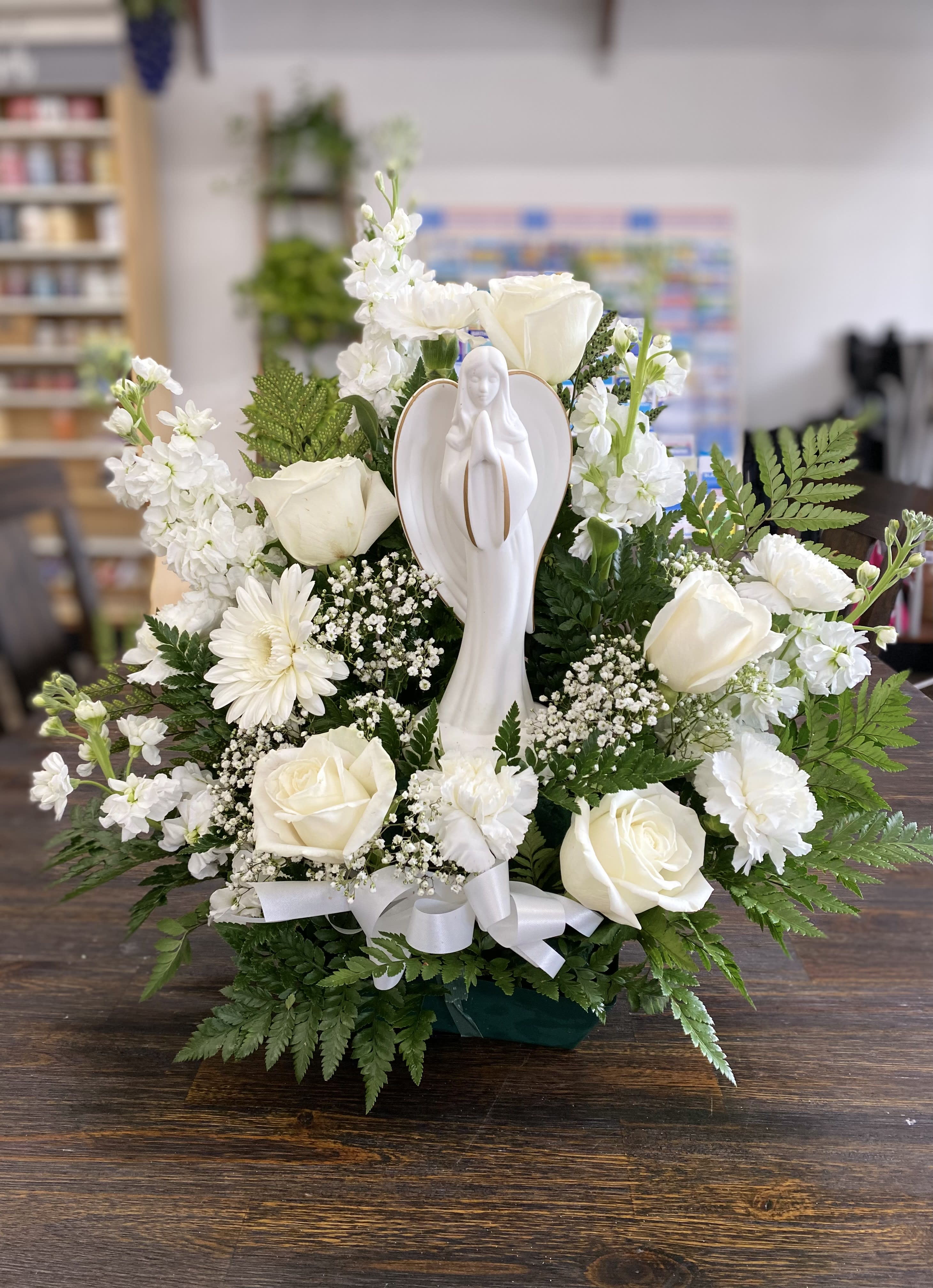 White roses and daisies arranged around a praying angel figurine