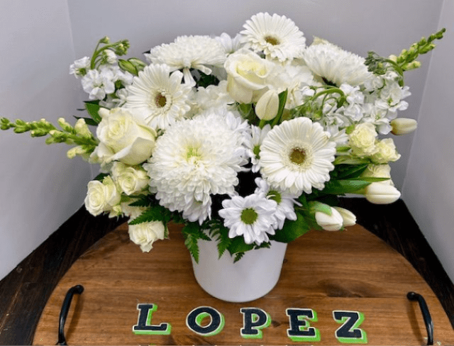 White flowers arranged in a white vase on a wooden tray