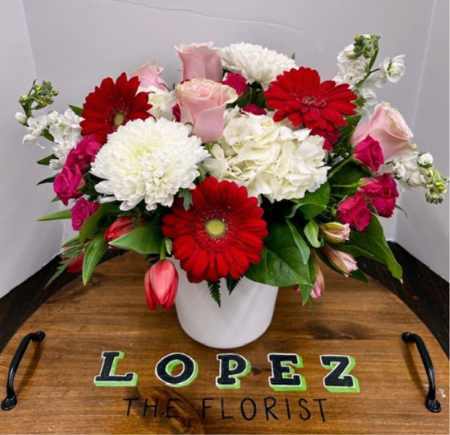 Bouquet of red gerbera daisies, pink roses, and white blooms in a white vase