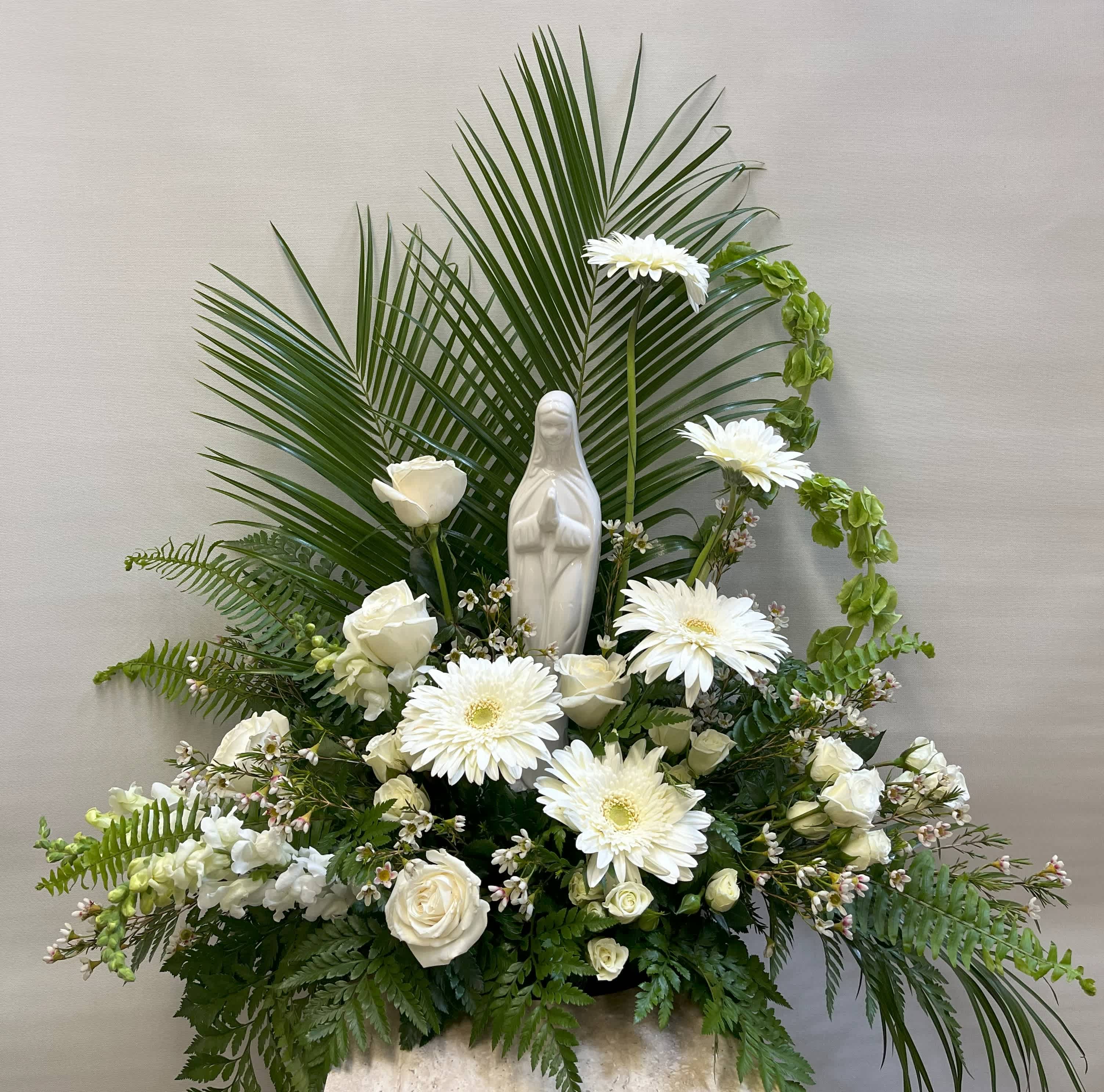 White floral arrangement with a small statue of the Virgin Mary