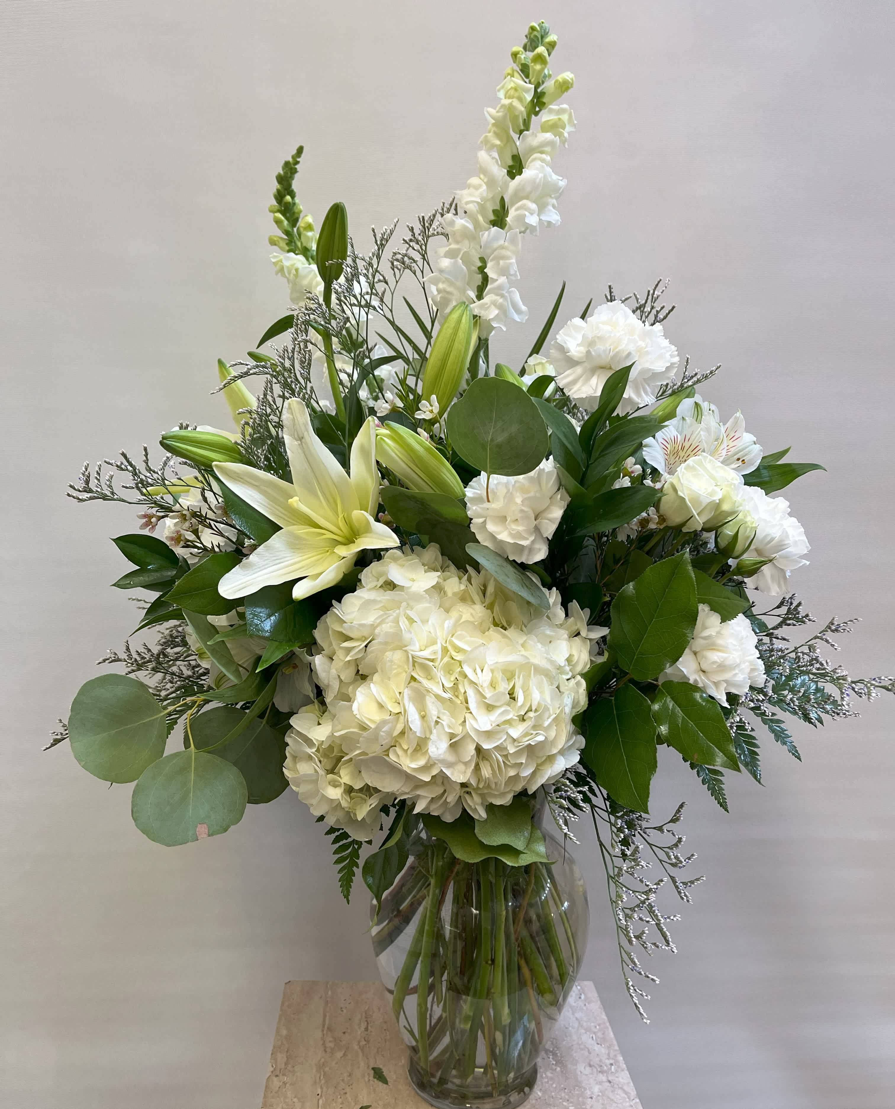 White floral arrangement in a clear glass vase with lilies and hydrangea