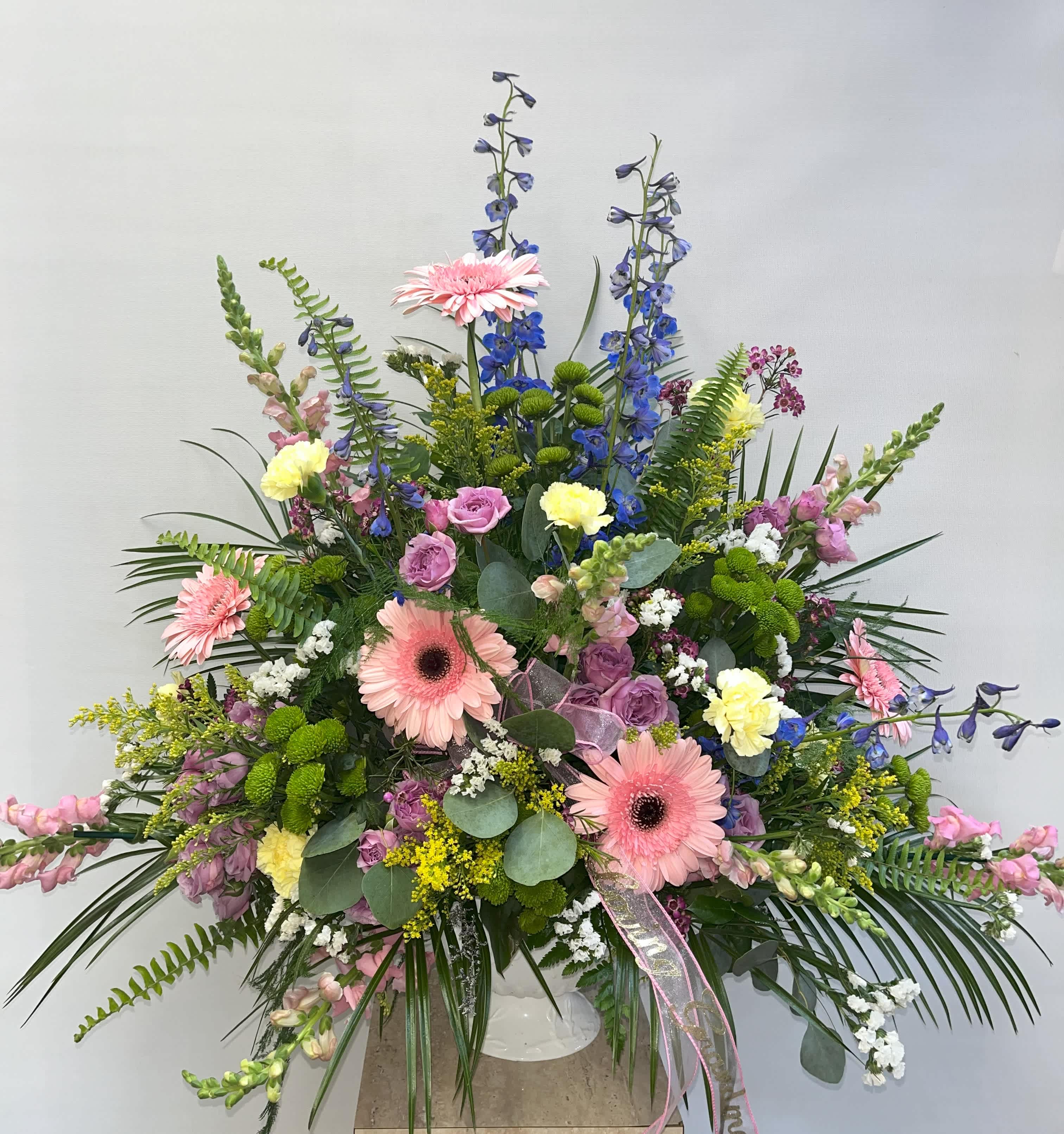 Large mixed floral arrangement with pink gerberas and blue delphinium in a white vase