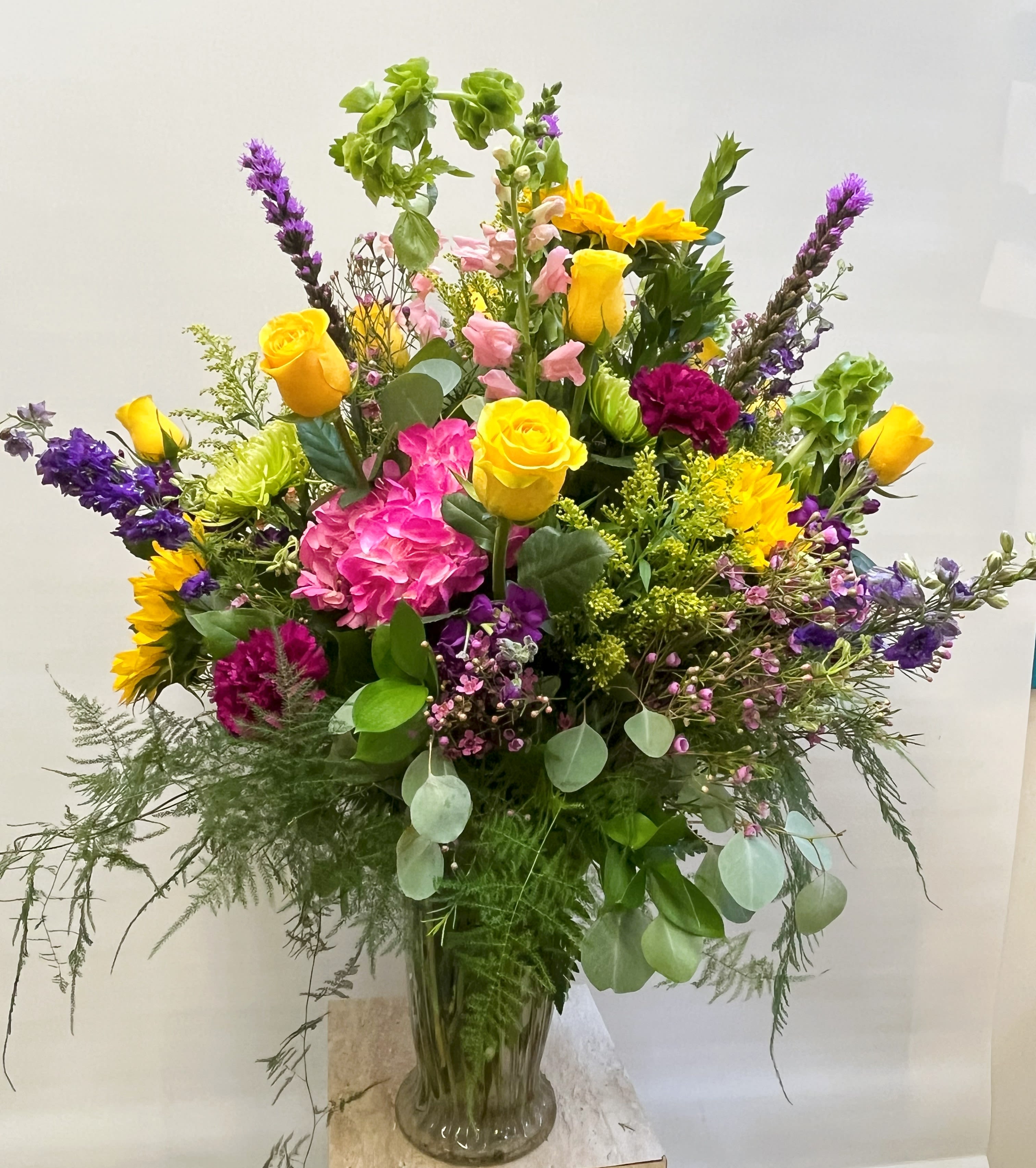 Mixed bouquet of yellow roses, pink hydrangea, and purple flowers in a glass vase