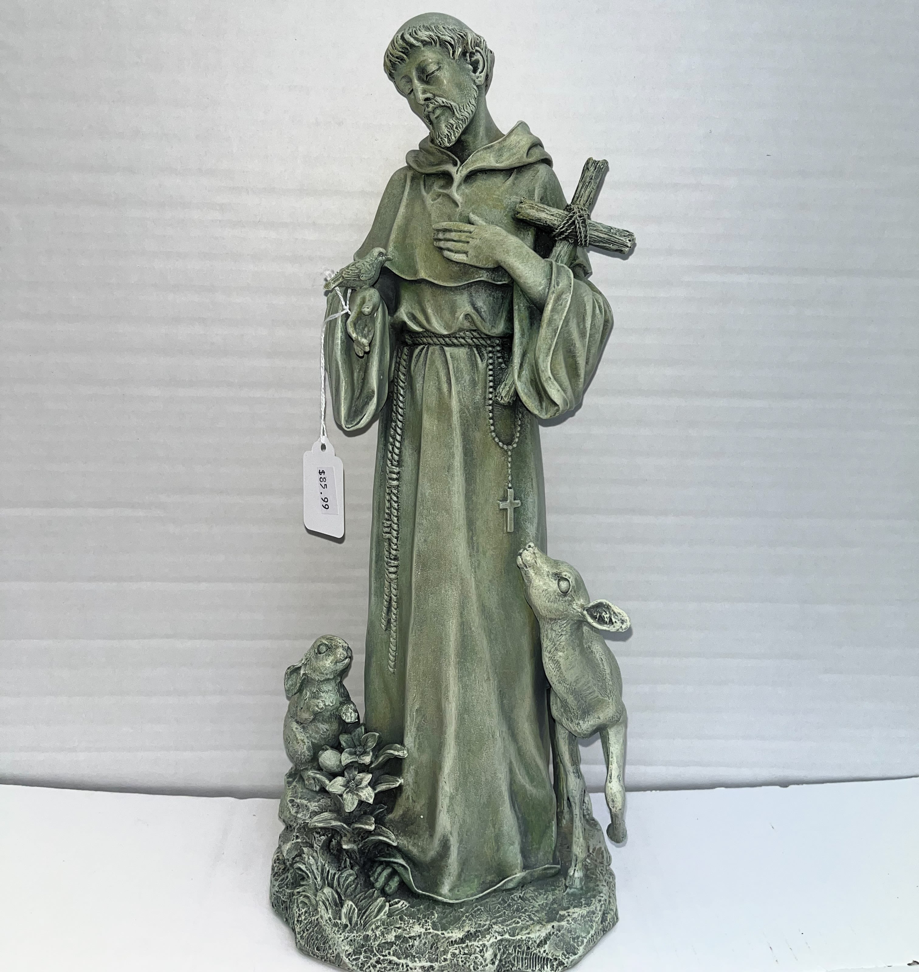 Green religious statue of a saint with a cross and two animals at the base