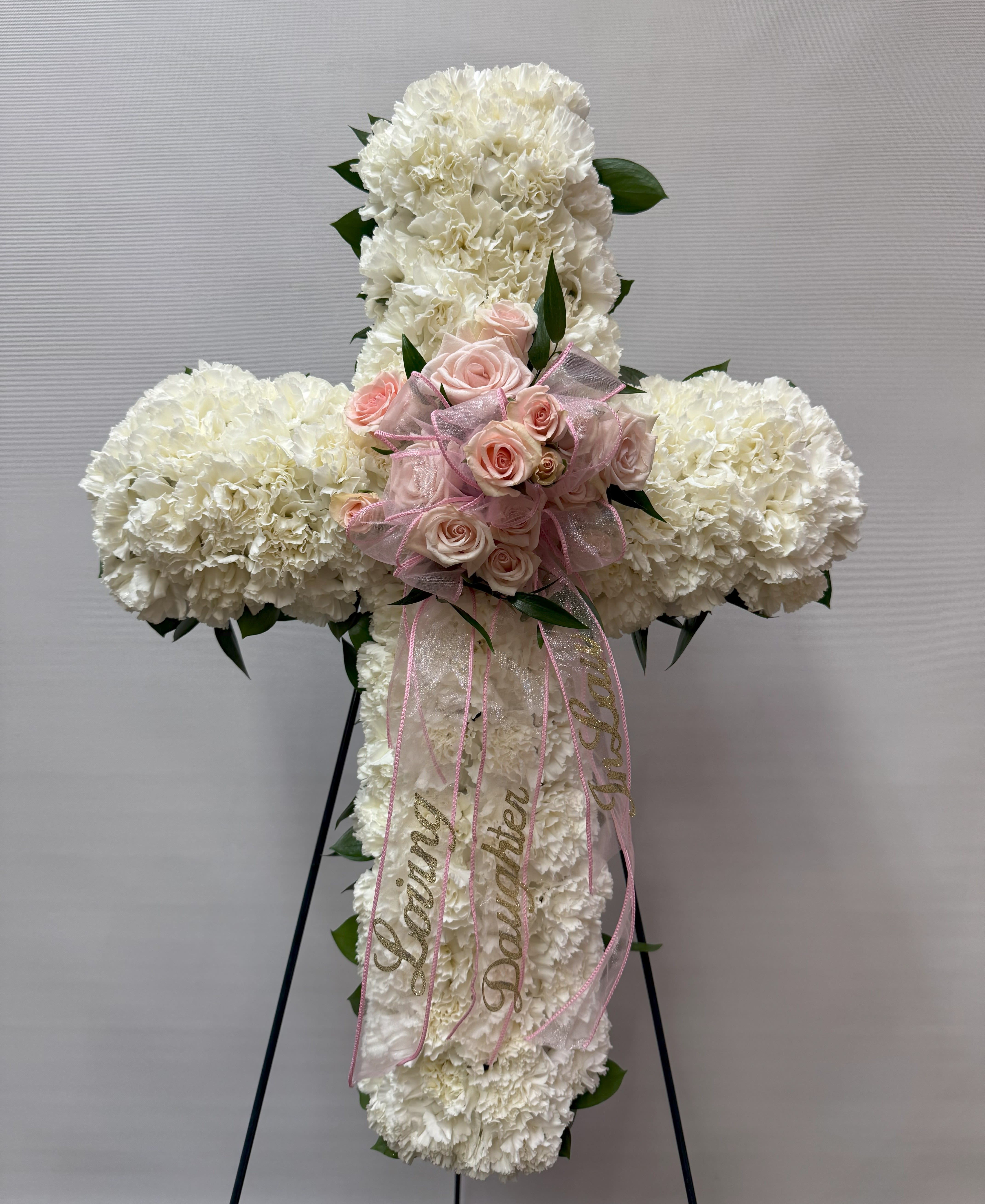 White floral cross with pink roses and ribbon on a stand