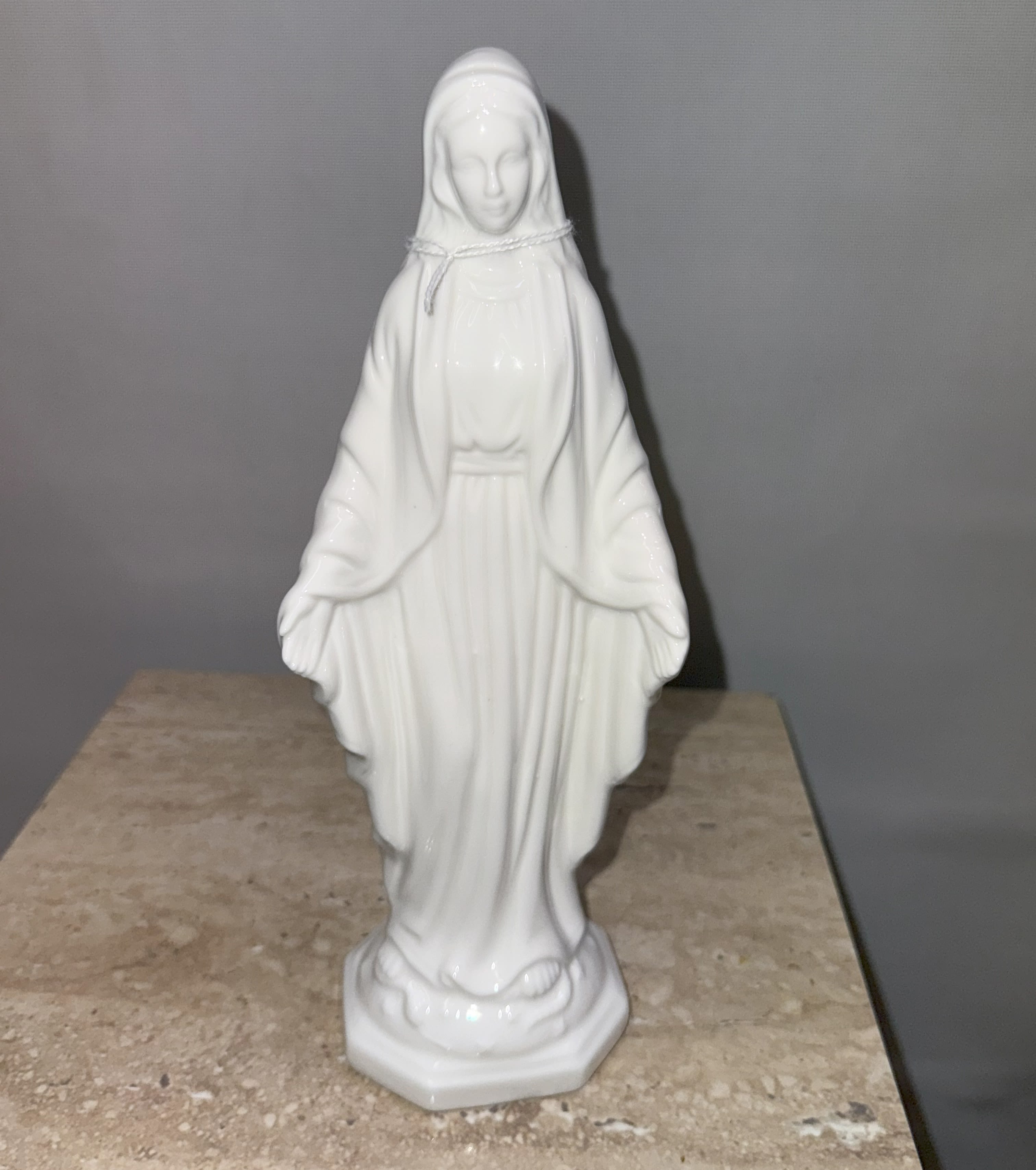 White religious statue of a robed woman standing on a base