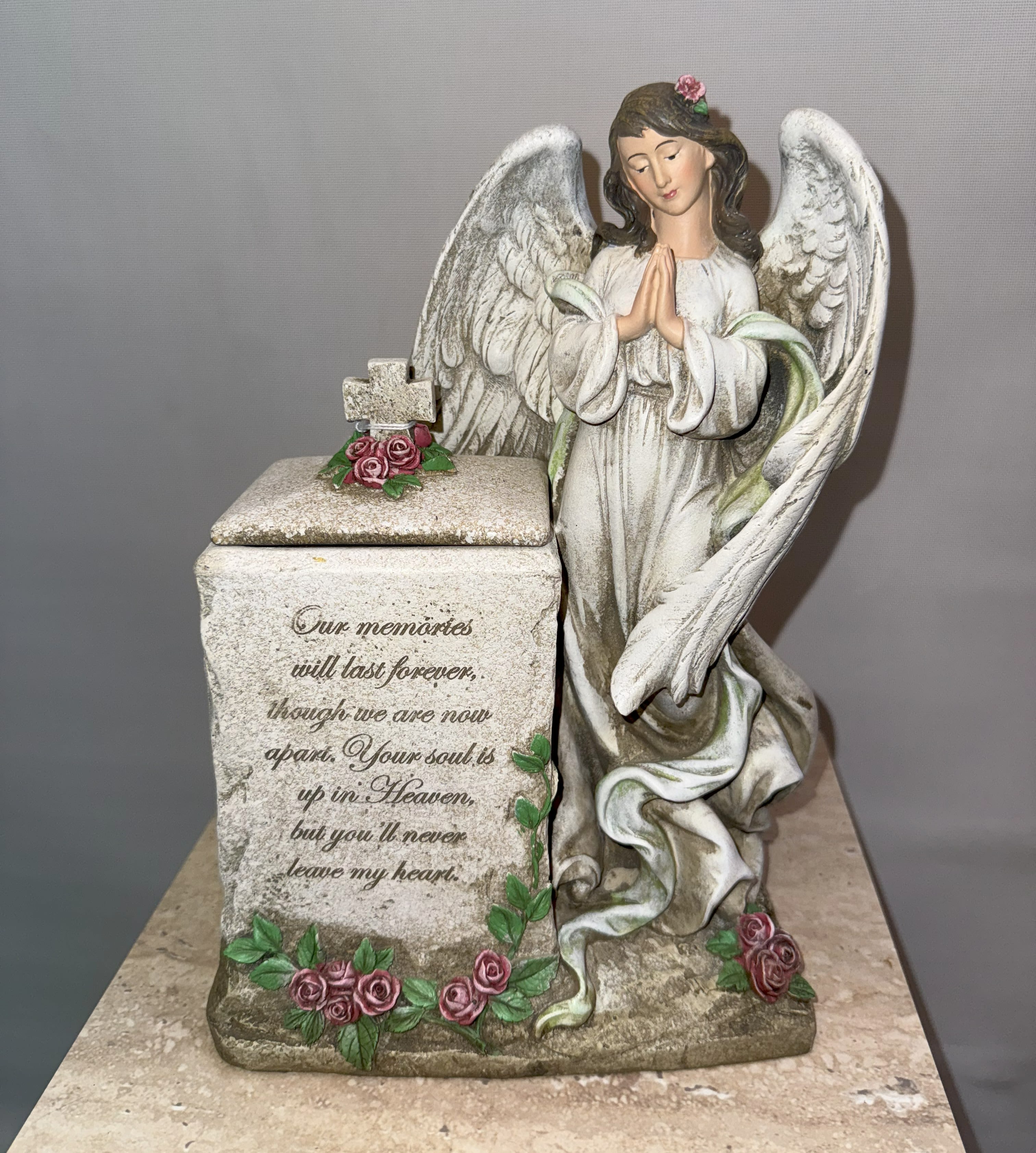 Angel figurine beside a memorial box decorated with pink roses