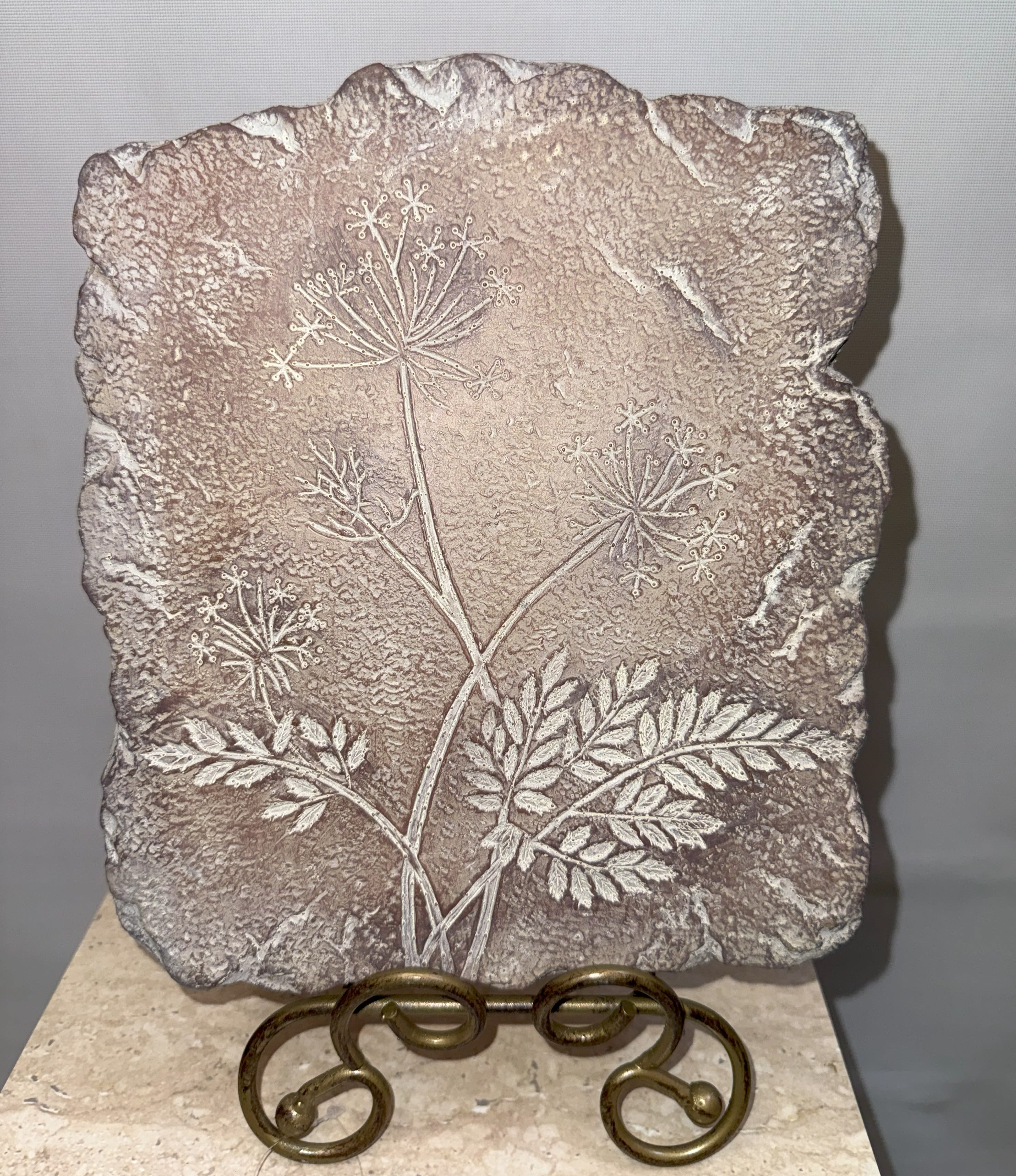 Textured stone plaque with an etched floral stem design on a metal stand