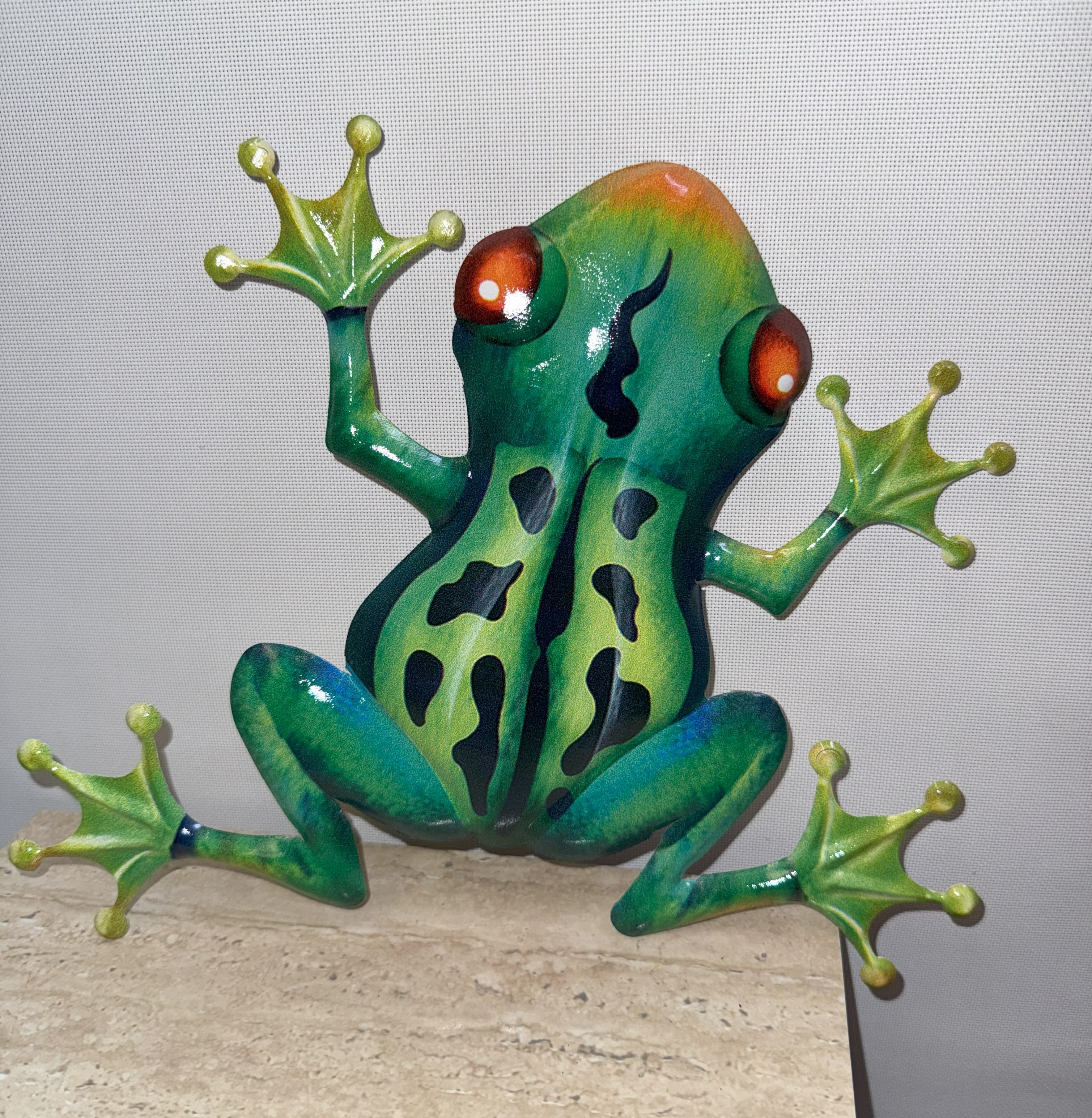 Colorful frog figurine with outstretched legs on a stone surface