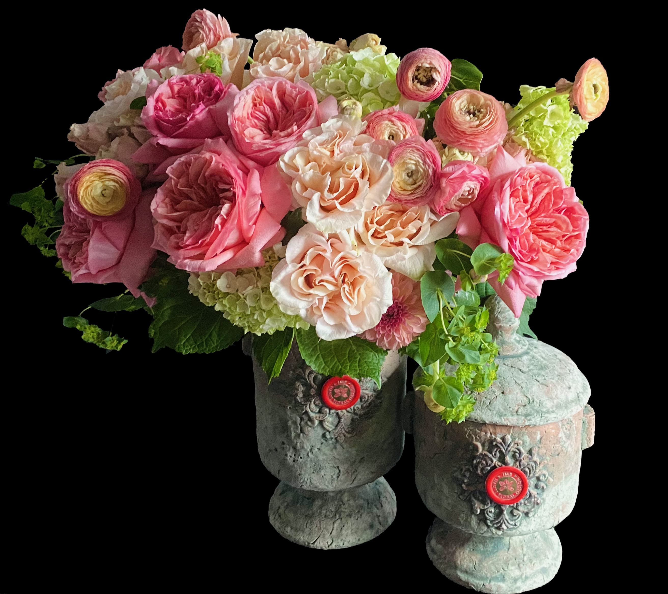 Lush arrangement of pink and peach roses, ranunculus, and hydrangeas in two rustic stone urn vases.