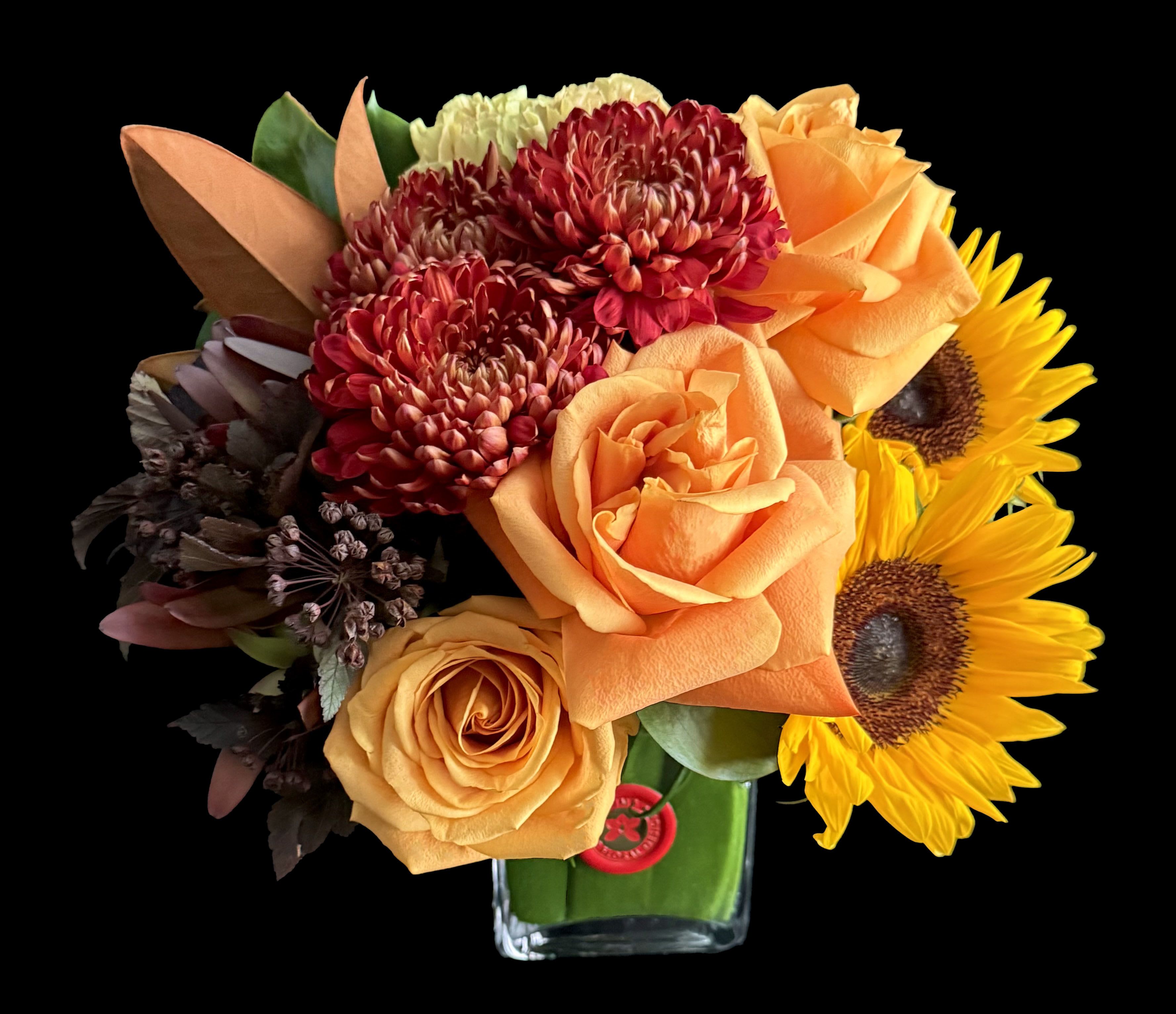 Orange roses, red chrysanthemums, and sunflowers in a glass vase