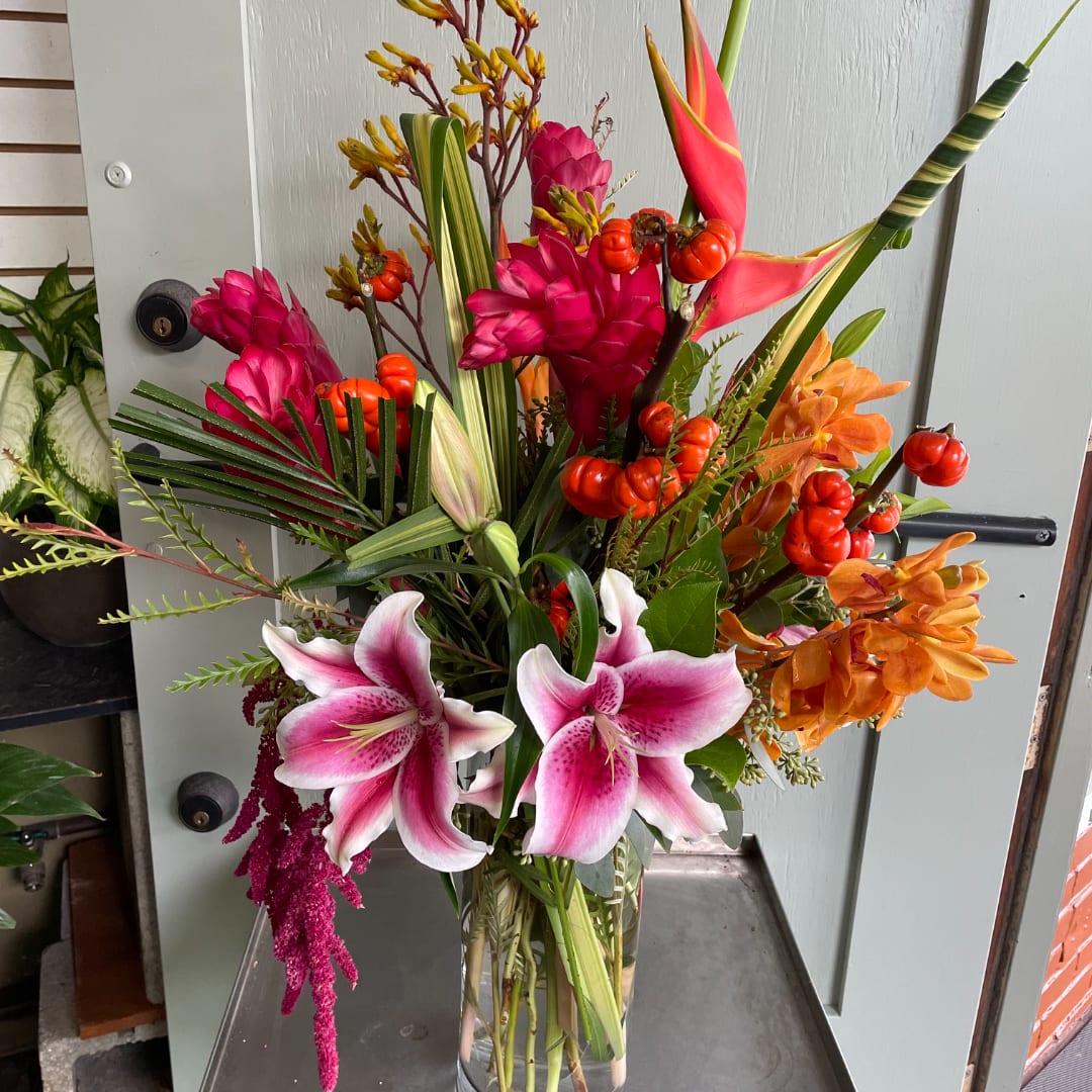 Tropical bouquet with pink lilies and orange flowers in a glass vase