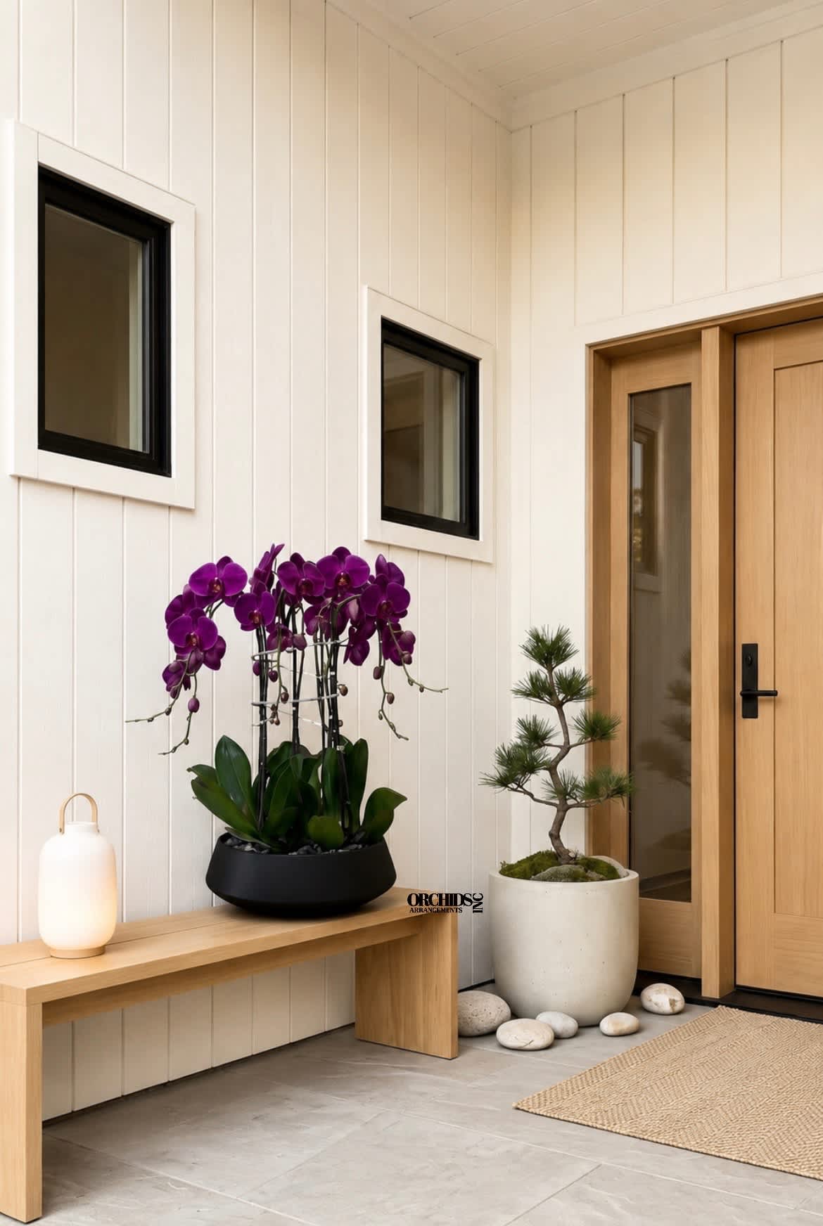Purple orchids in a black planter beside a small potted tree and lantern