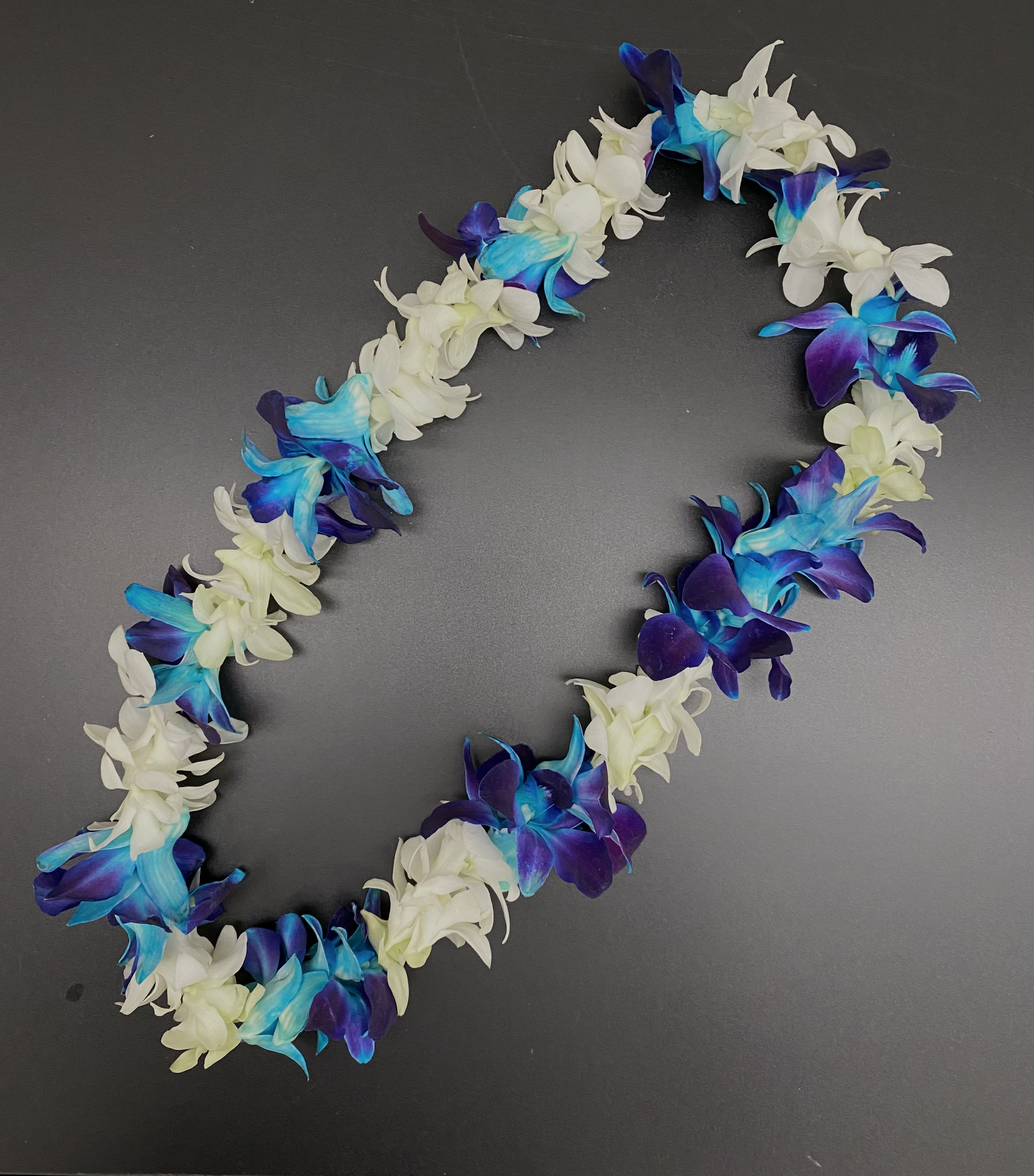 Flower lei with white, blue, and purple blossoms on a dark background