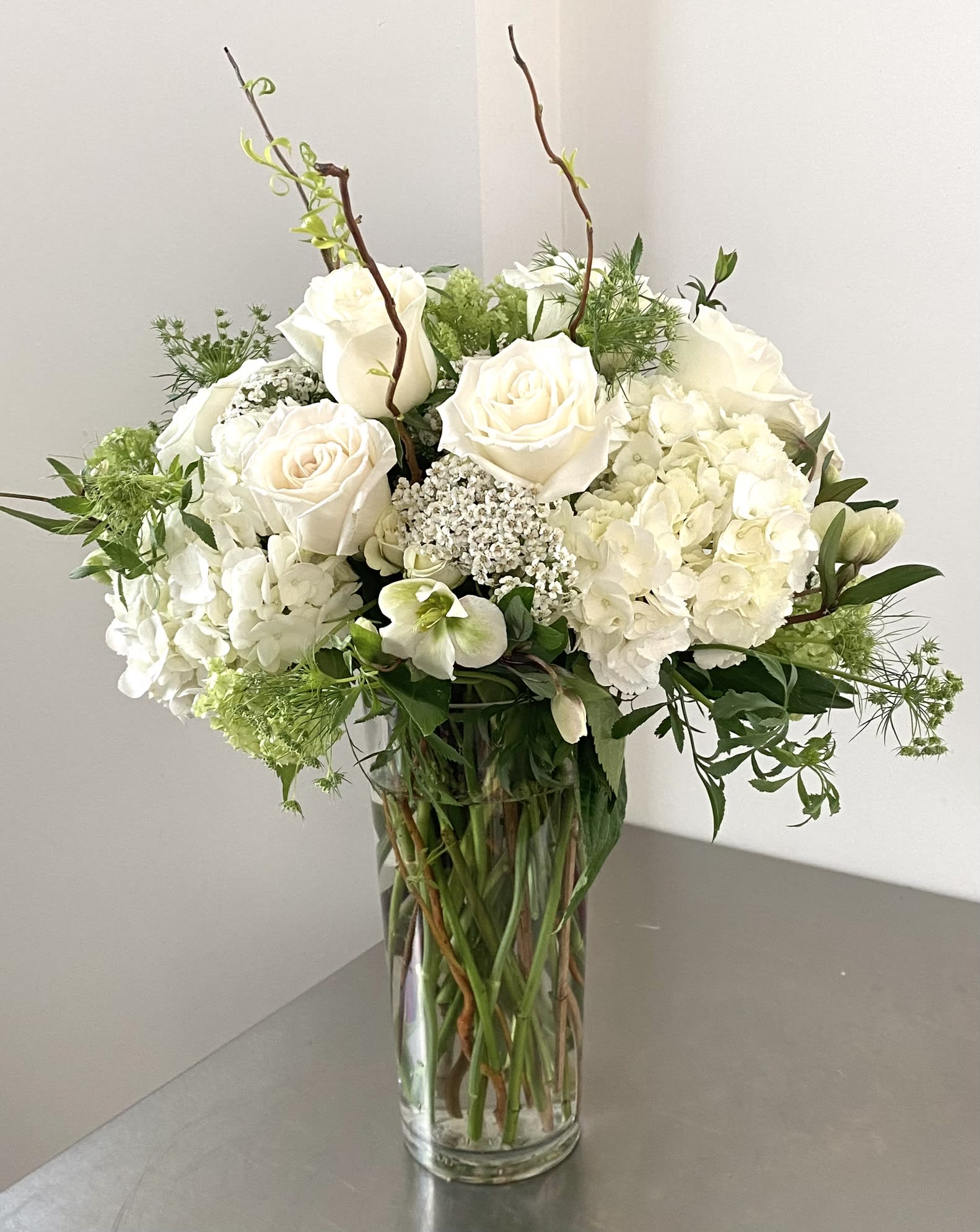 White roses and hydrangeas in a clear glass vase with greenery