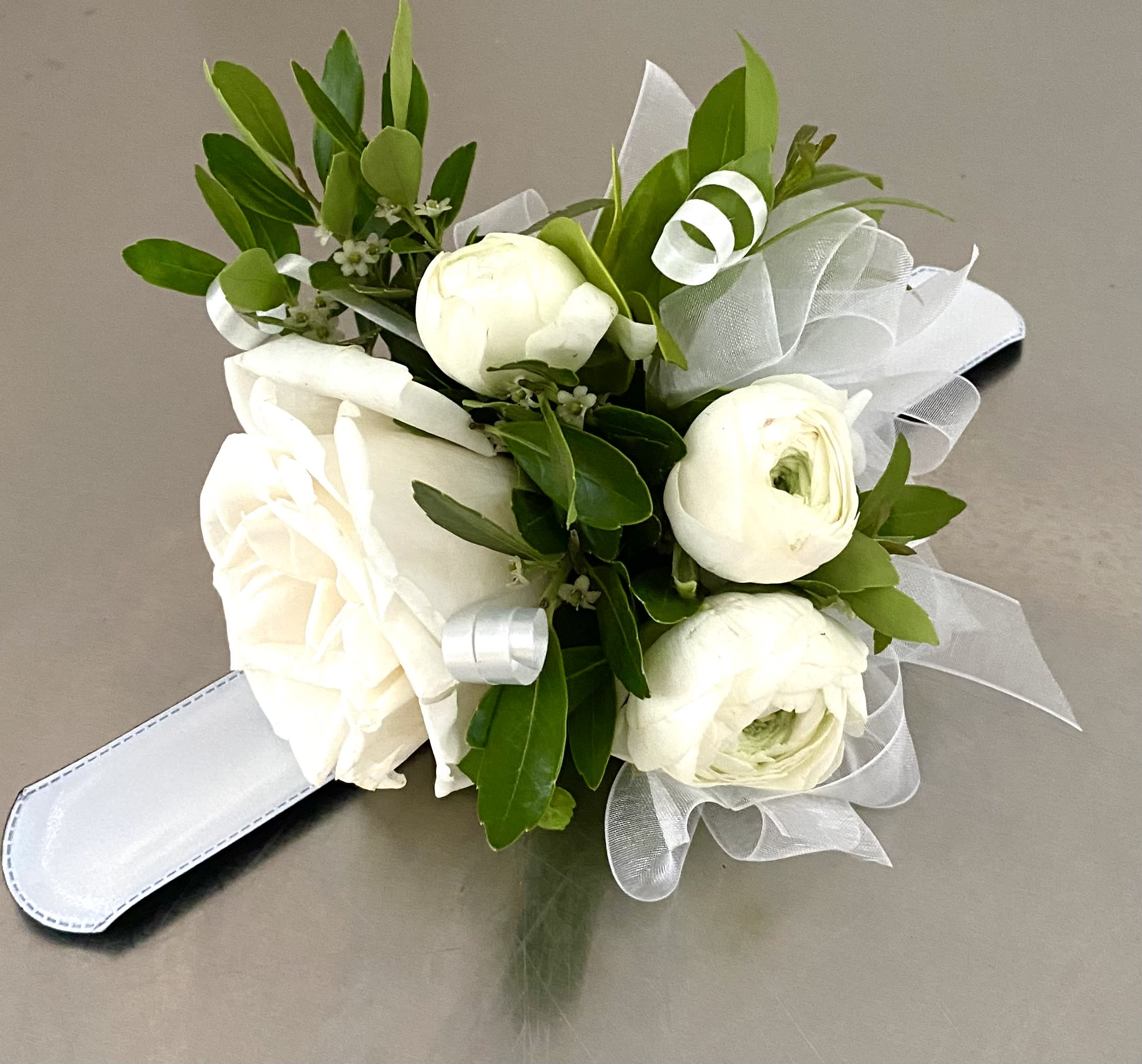 White rose and ranunculus bouquet with green foliage and white ribbon