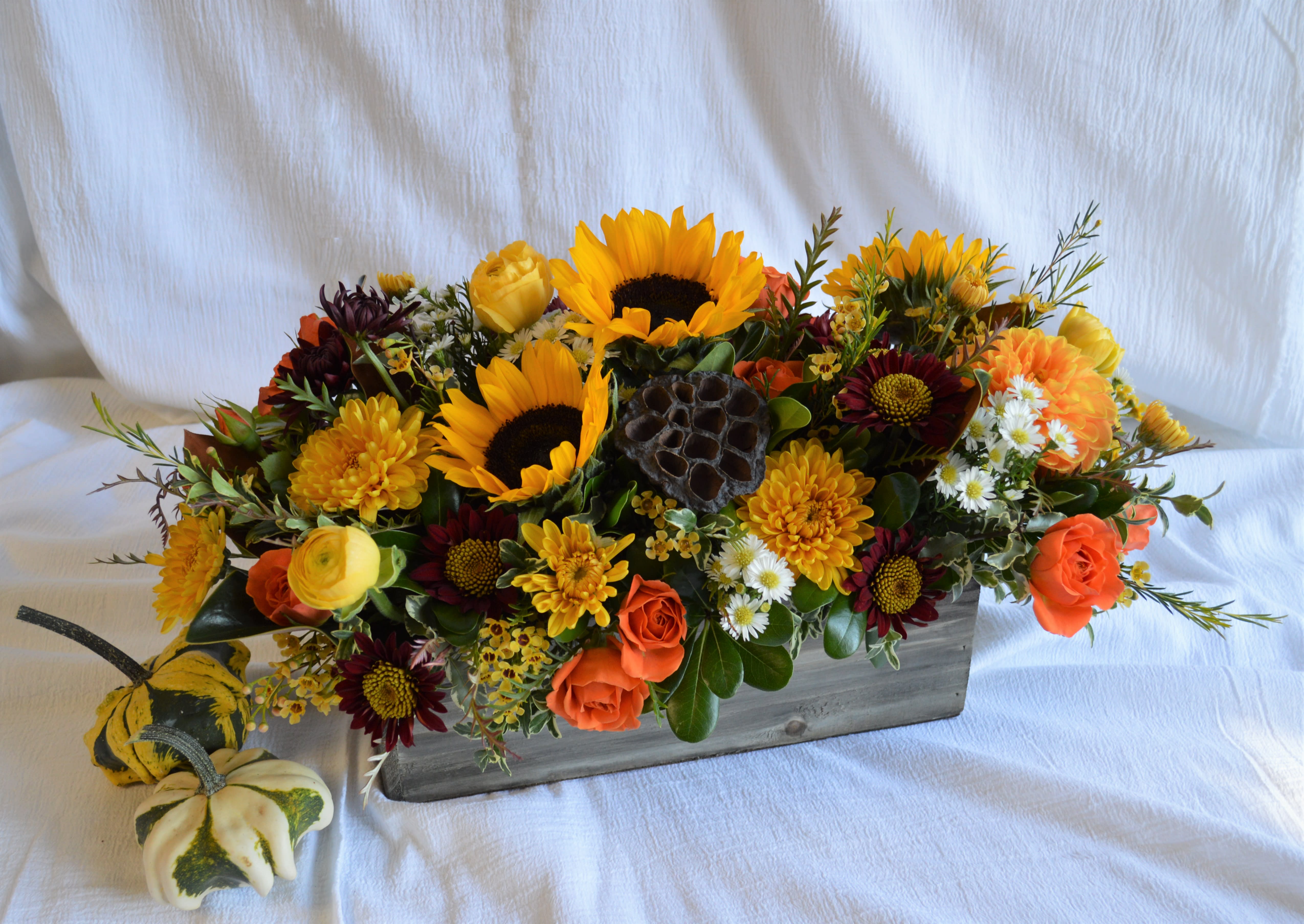 Woodland Centerpiece - A lush centerpiece full of berries, lotus pods, seasonal foliage and fresh fall flowers arranged in a long wooden box. We love to create custom color palettes for our customers. If you prefer a particular palette such as cool colors (purples, blues) or would like brighter more vibrant colors (saturated yellows, oranges) or a darker moody palette - please note any specific color preferences in the 'special instructions' box. This arrangement is approximately 12" tall x 20" wide, but can be taller/wider if upgraded.
