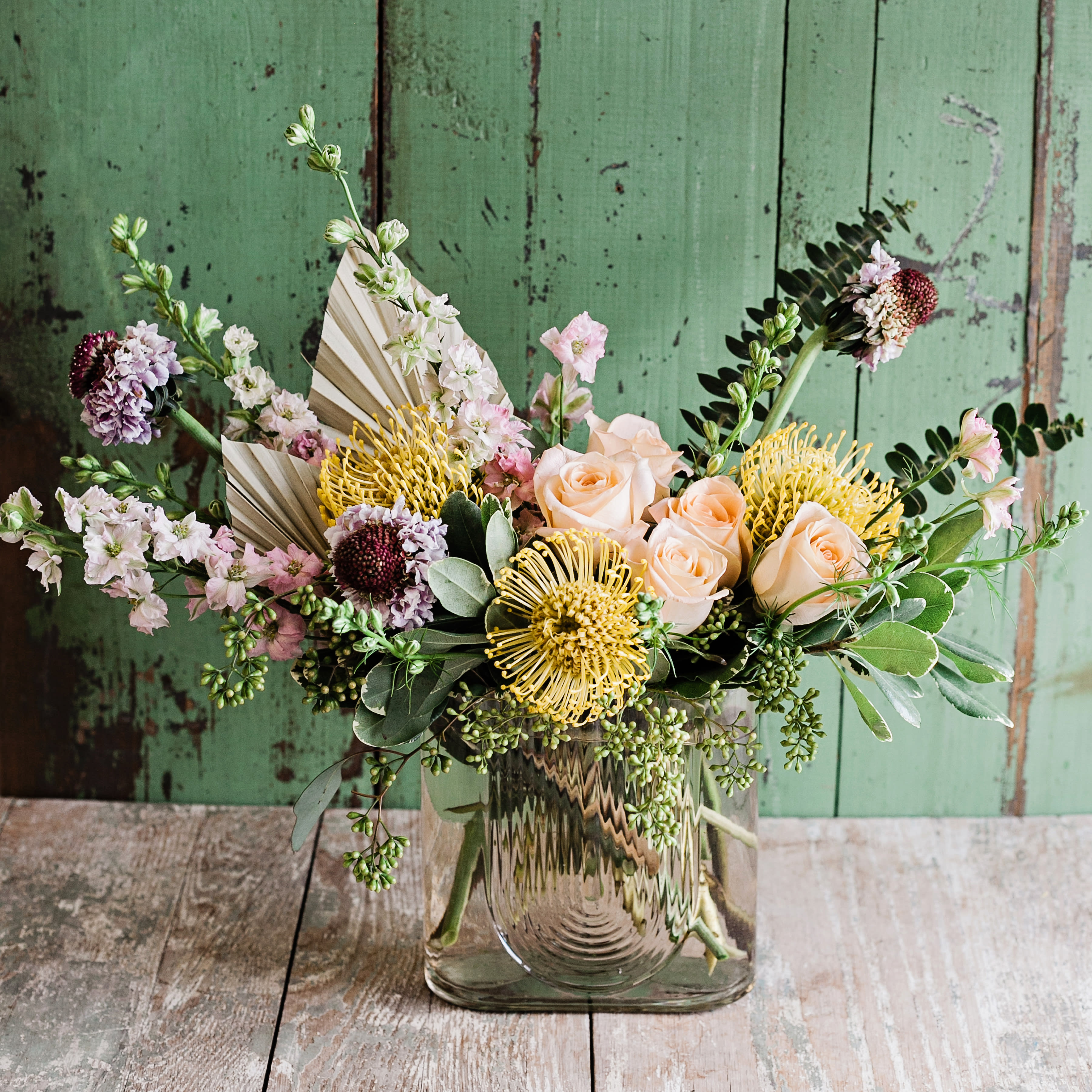 Mixed bouquet of peach roses and yellow pincushion blooms in a glass vase