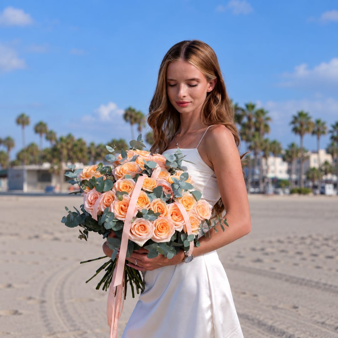 Woman in a white dress holding a bouquet of peach roses