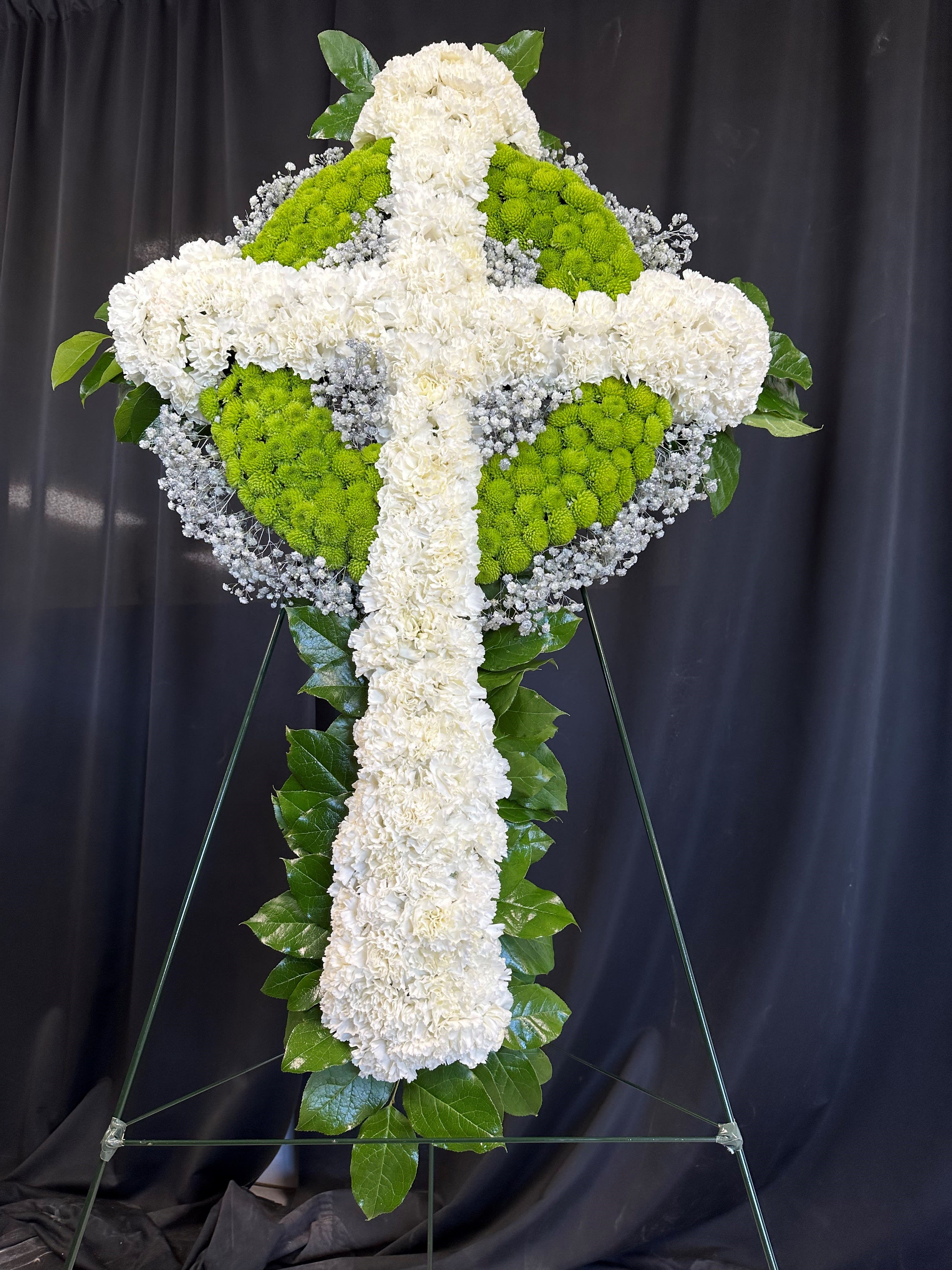 White and green floral cross on a stand against a dark backdrop