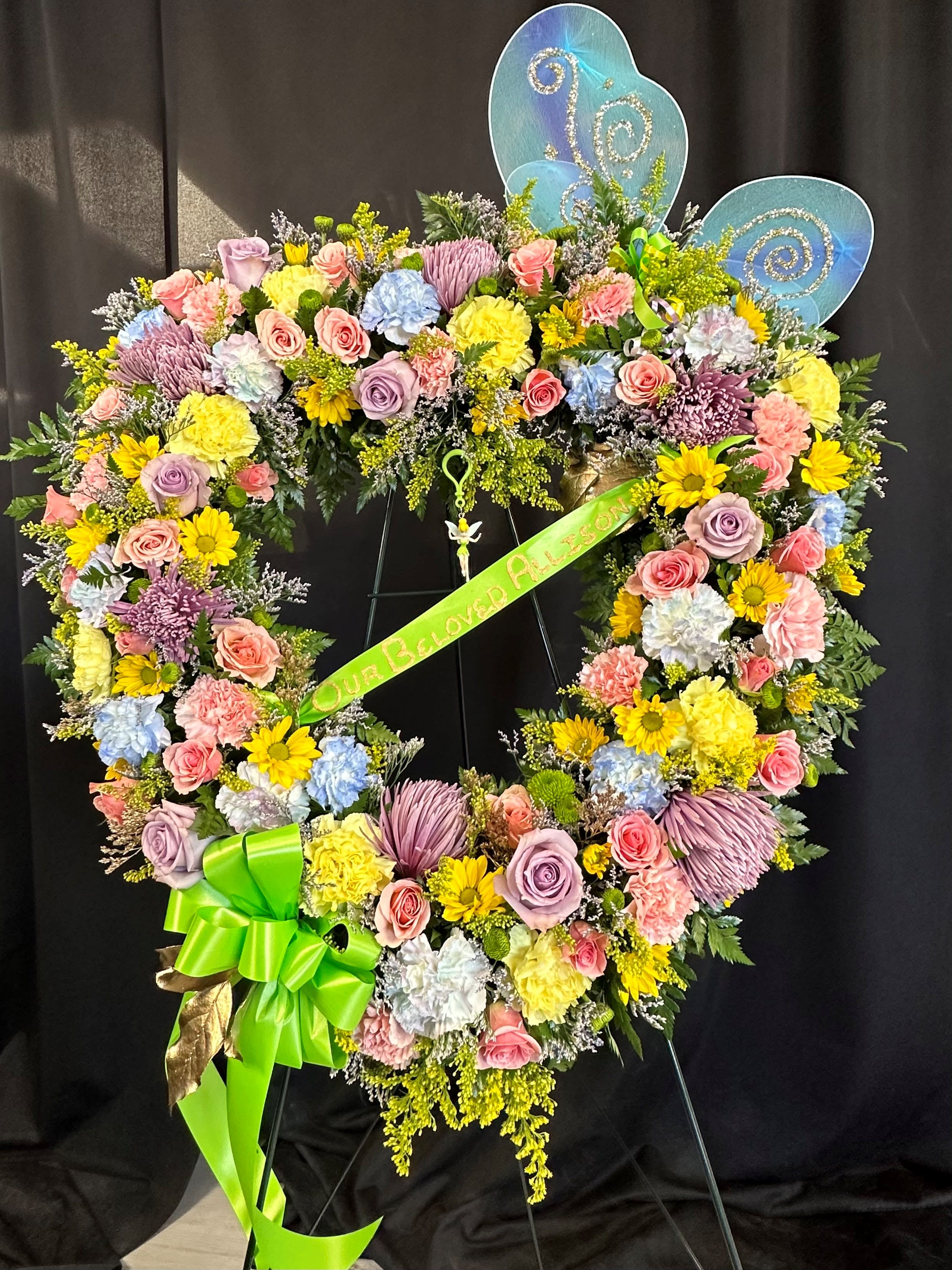Heart-shaped floral wreath with pastel flowers and a green ribbon