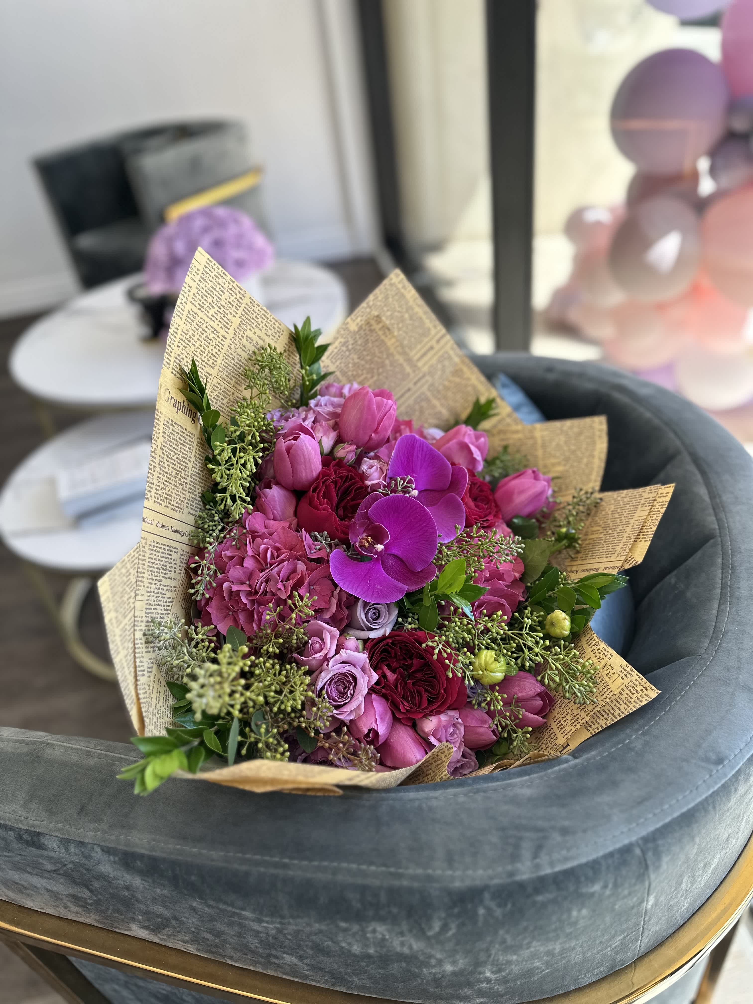 Pink and purple bouquet with roses and orchids wrapped in newspaper-style paper