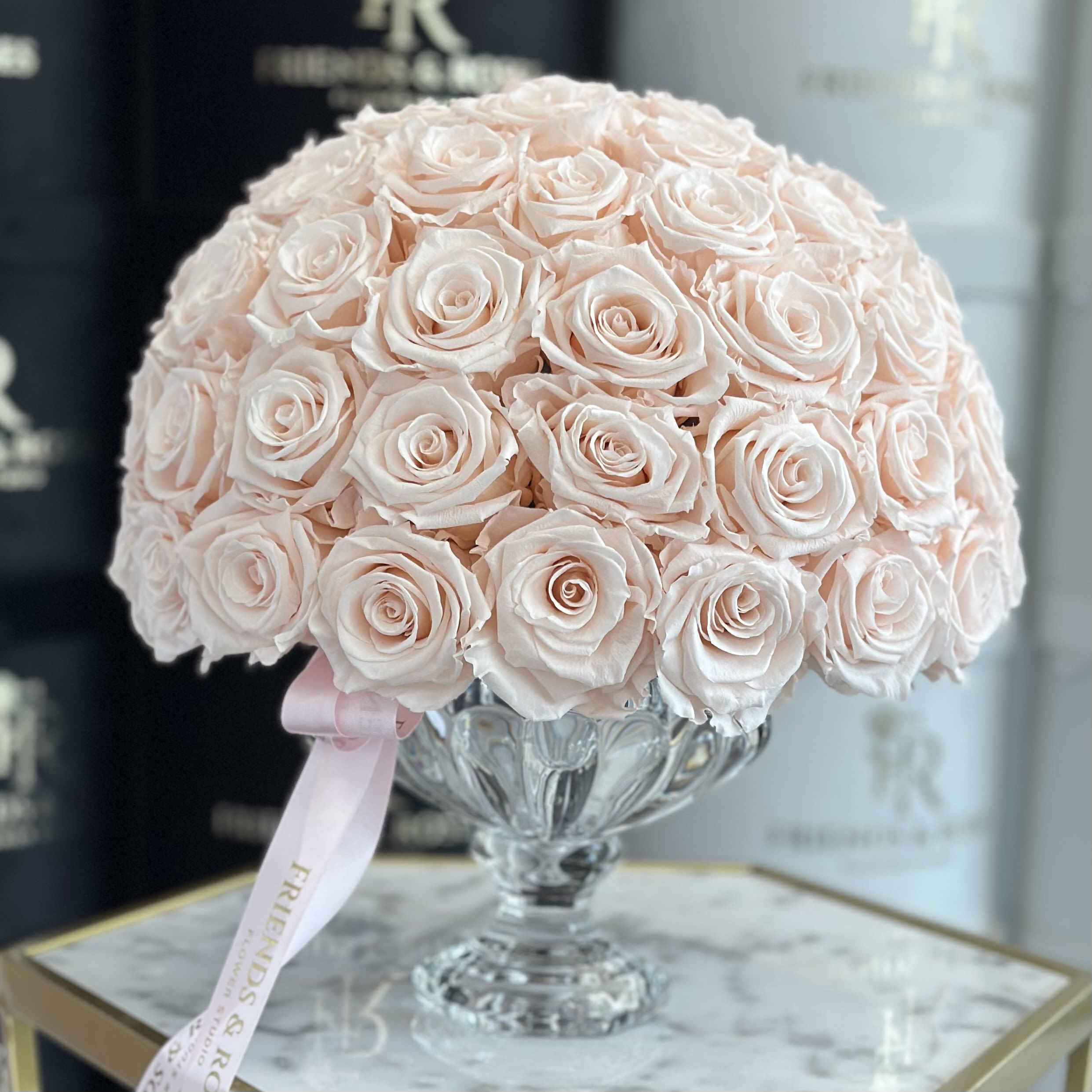 A dome of pale pink roses in a clear glass vase with a pink ribbon.