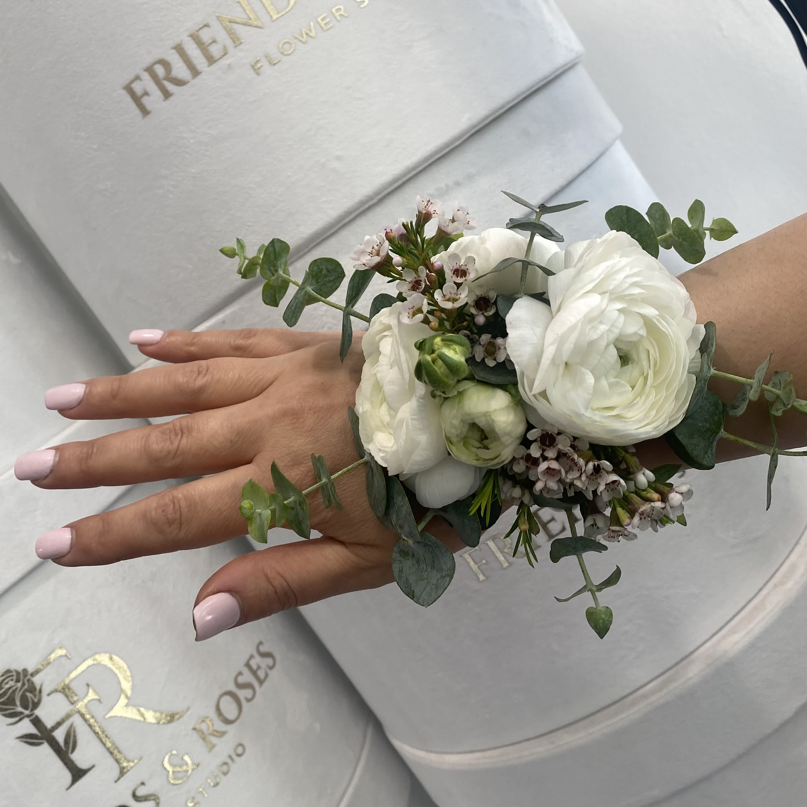 White floral wrist corsage with eucalyptus on a hand