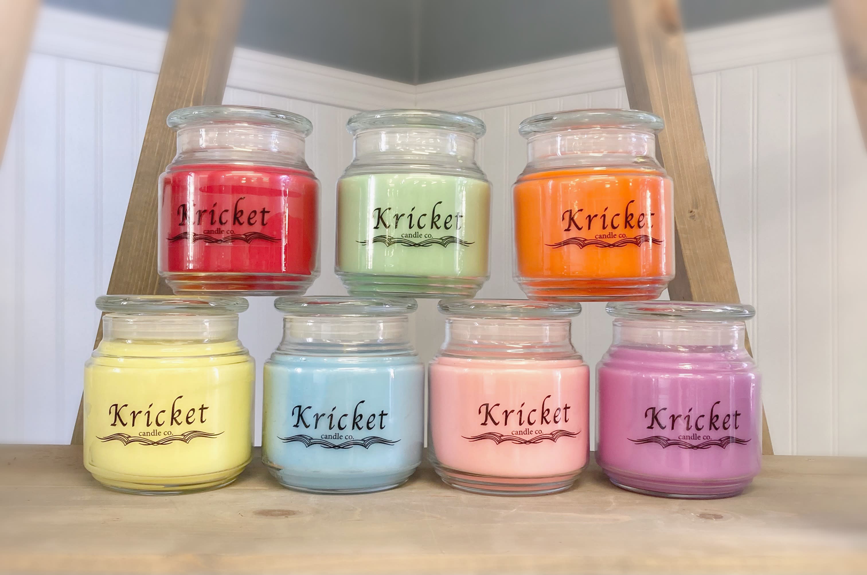 Seven colorful jar candles arranged on a wooden shelf
