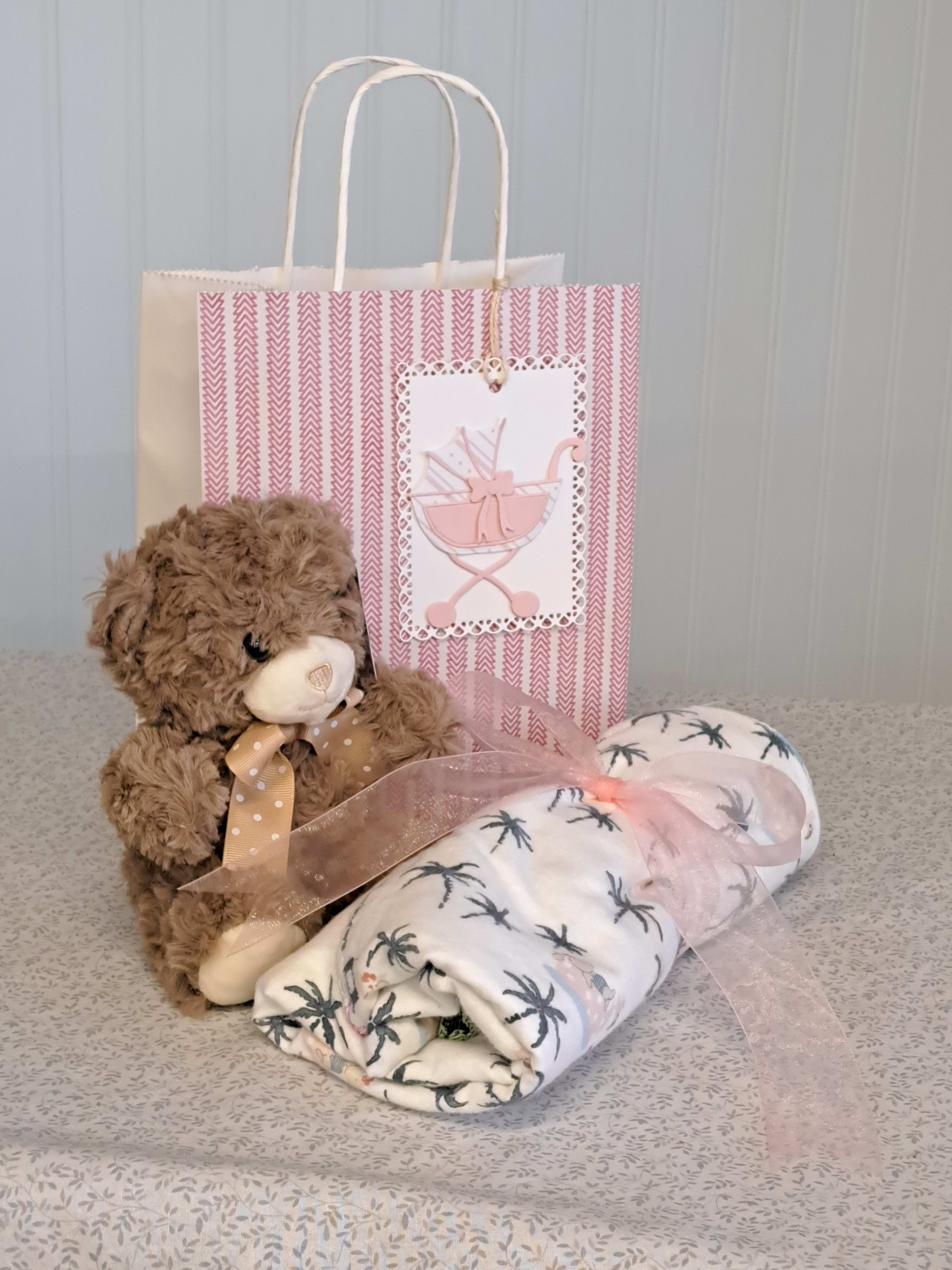 Teddy bear, rolled baby blanket, and gift bag with a pink card