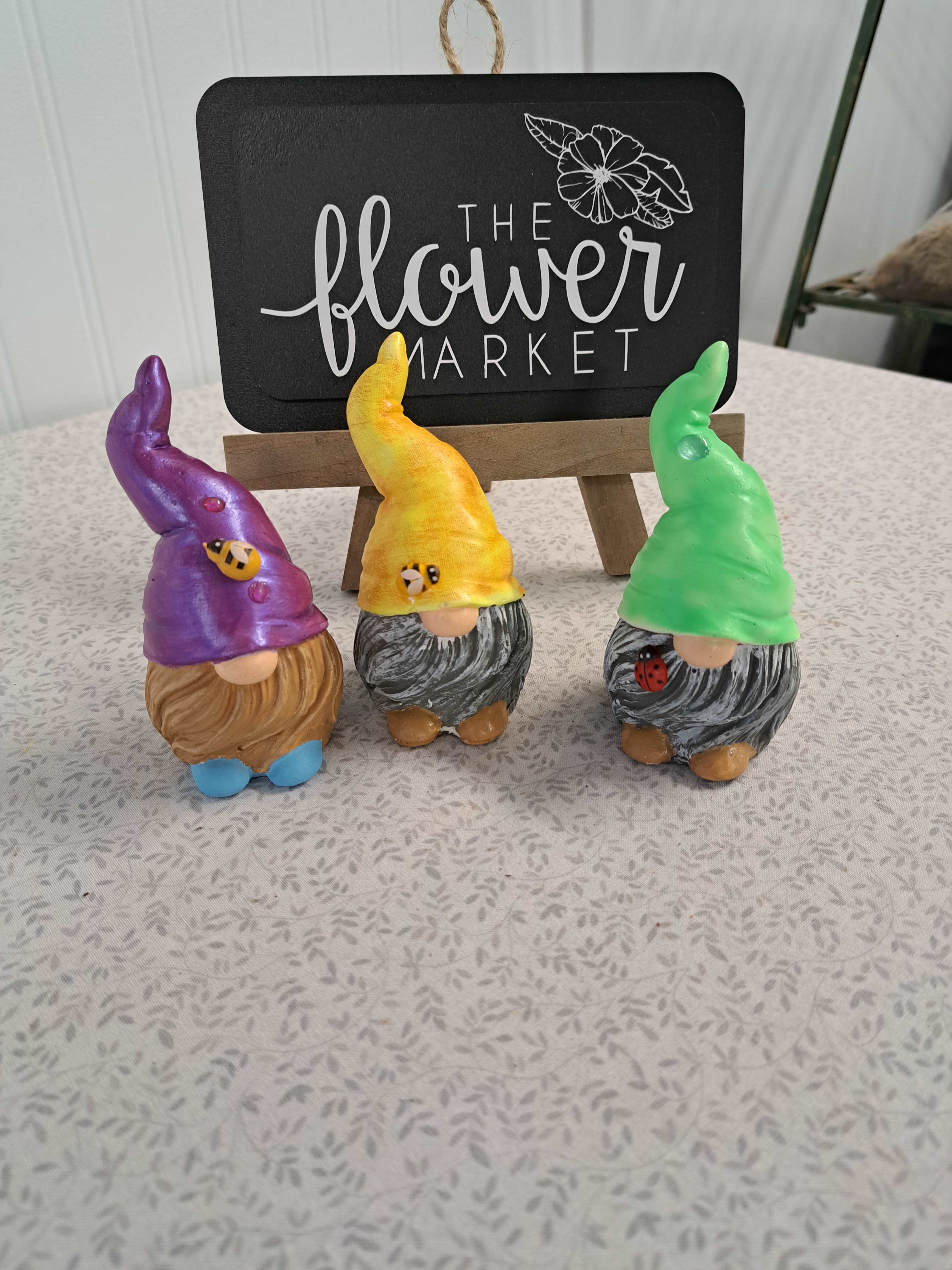 Three colorful gnome figurines displayed in front of a flower market sign