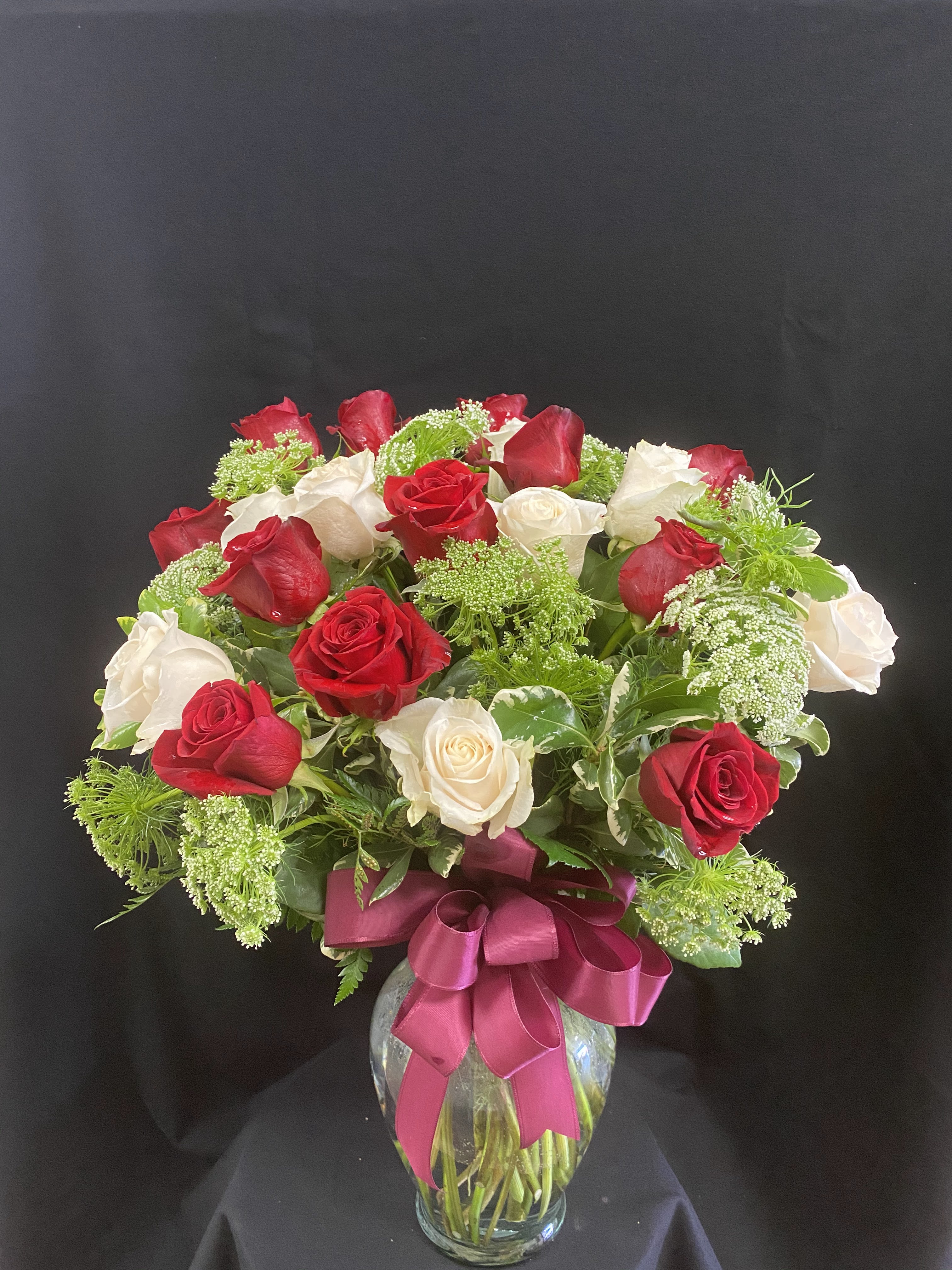 Red and white roses in a glass vase with a pink ribbon