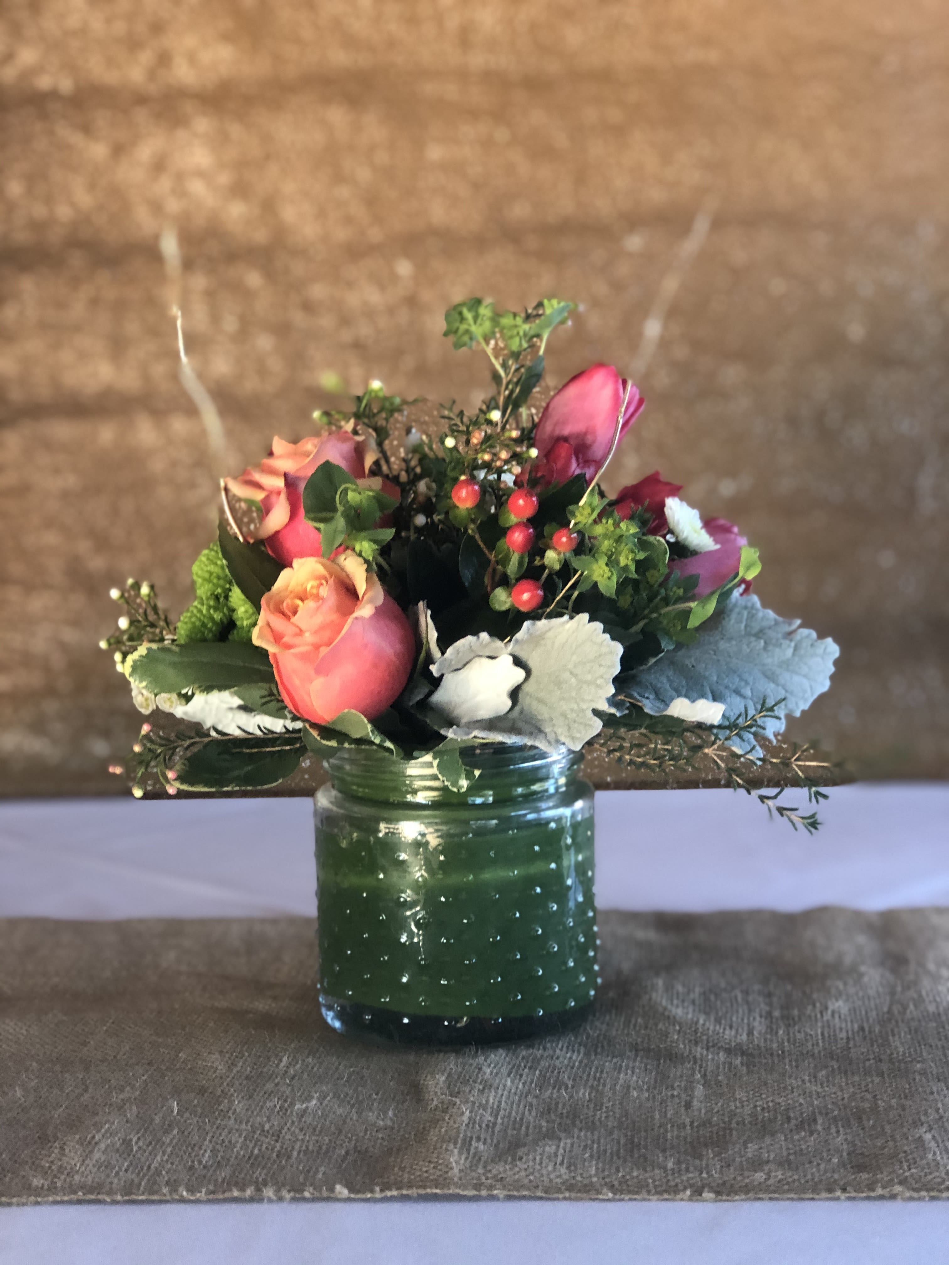 Pink roses in a green glass jar with berries and foliage